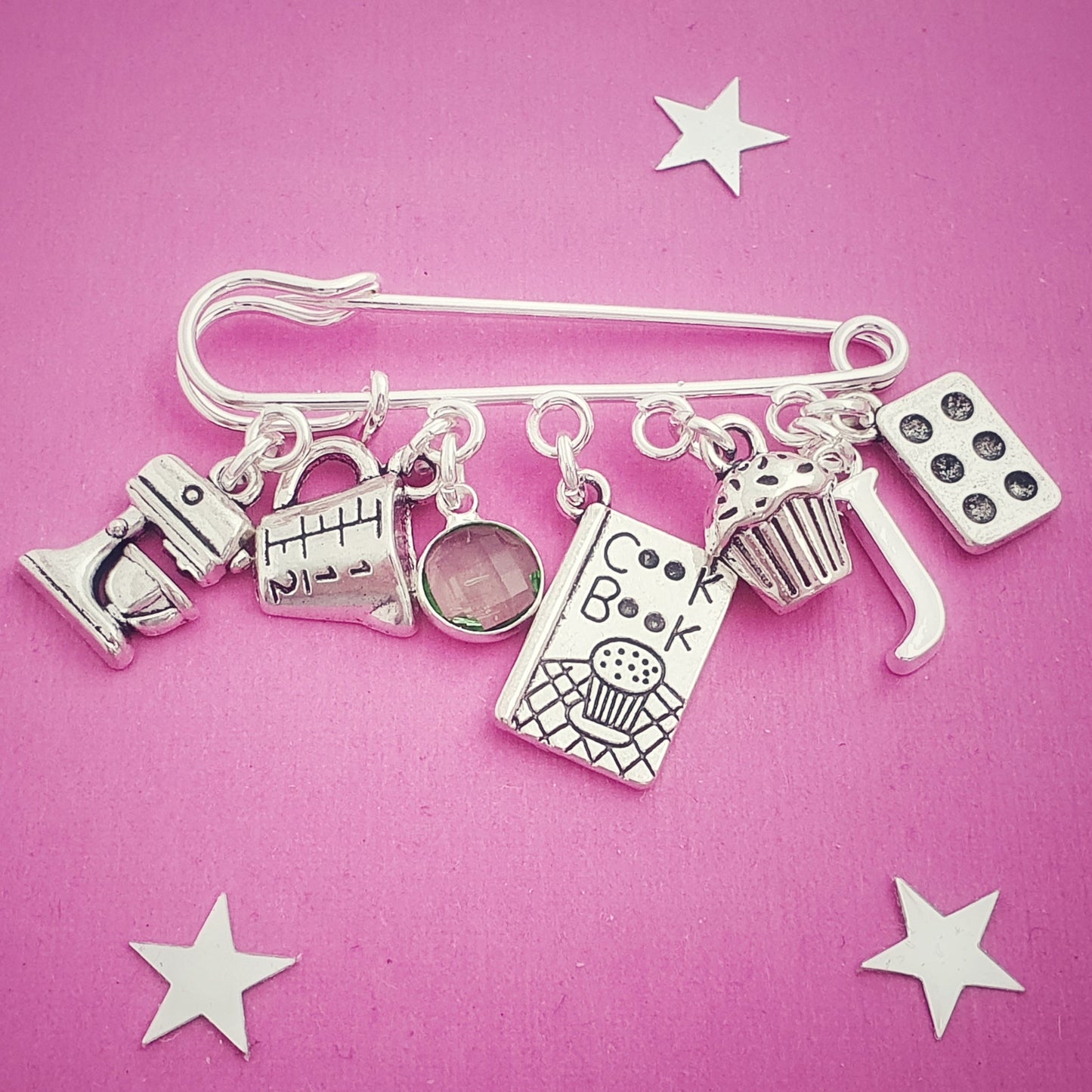 Silver charm brooch with various cooking charms on a pink background with star decorations