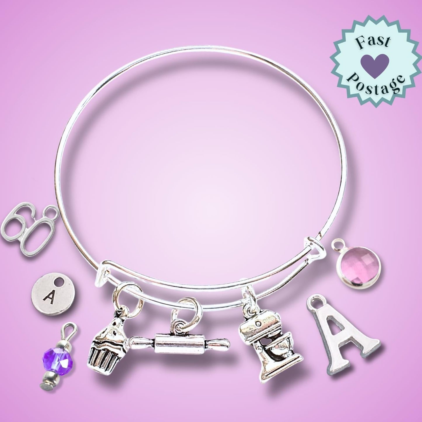 A silver-toned expandable bangle bracelet with multiple charms, including letters, a cupcake, a rolling pin, a mixer, and a pink gem, displayed on a pink background with a 'Fast Postage' badge.