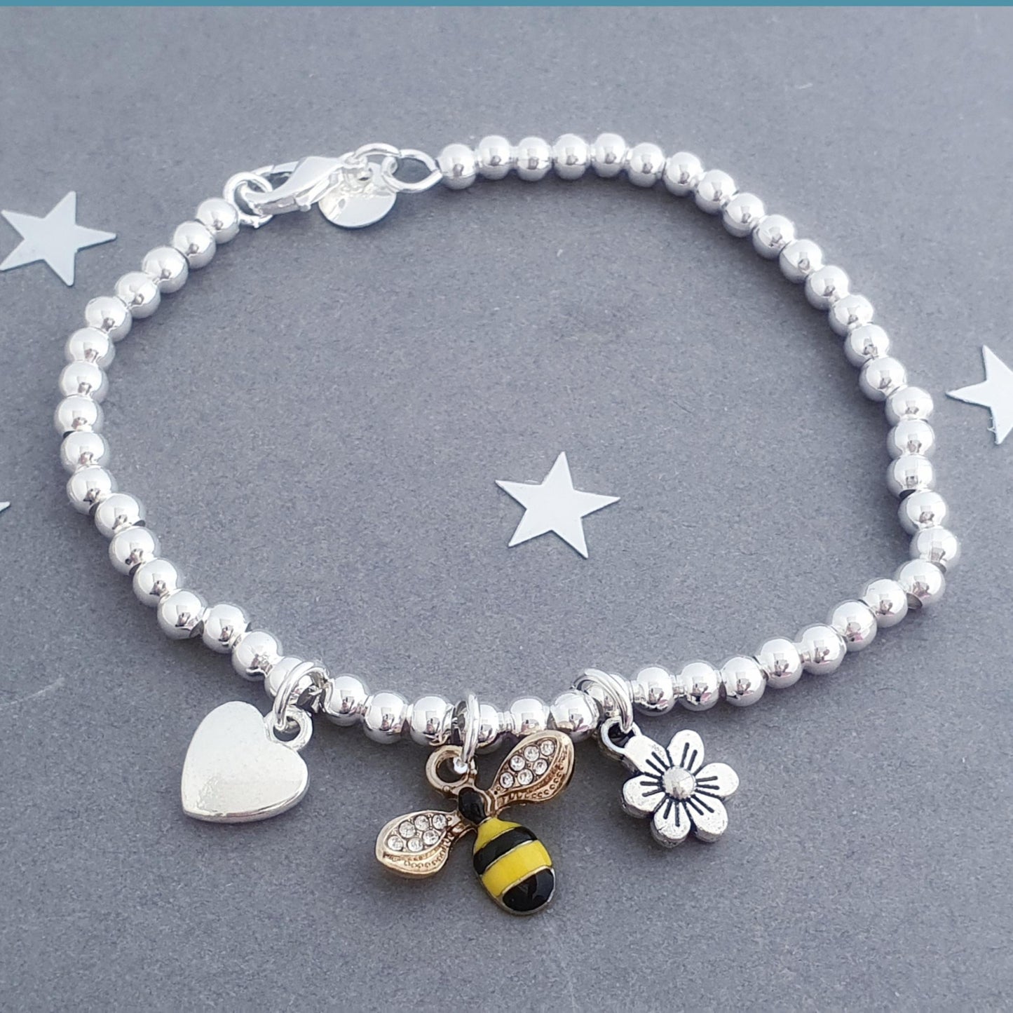 Sterling silver bracelet with bee, heart and flower charms on a grey background