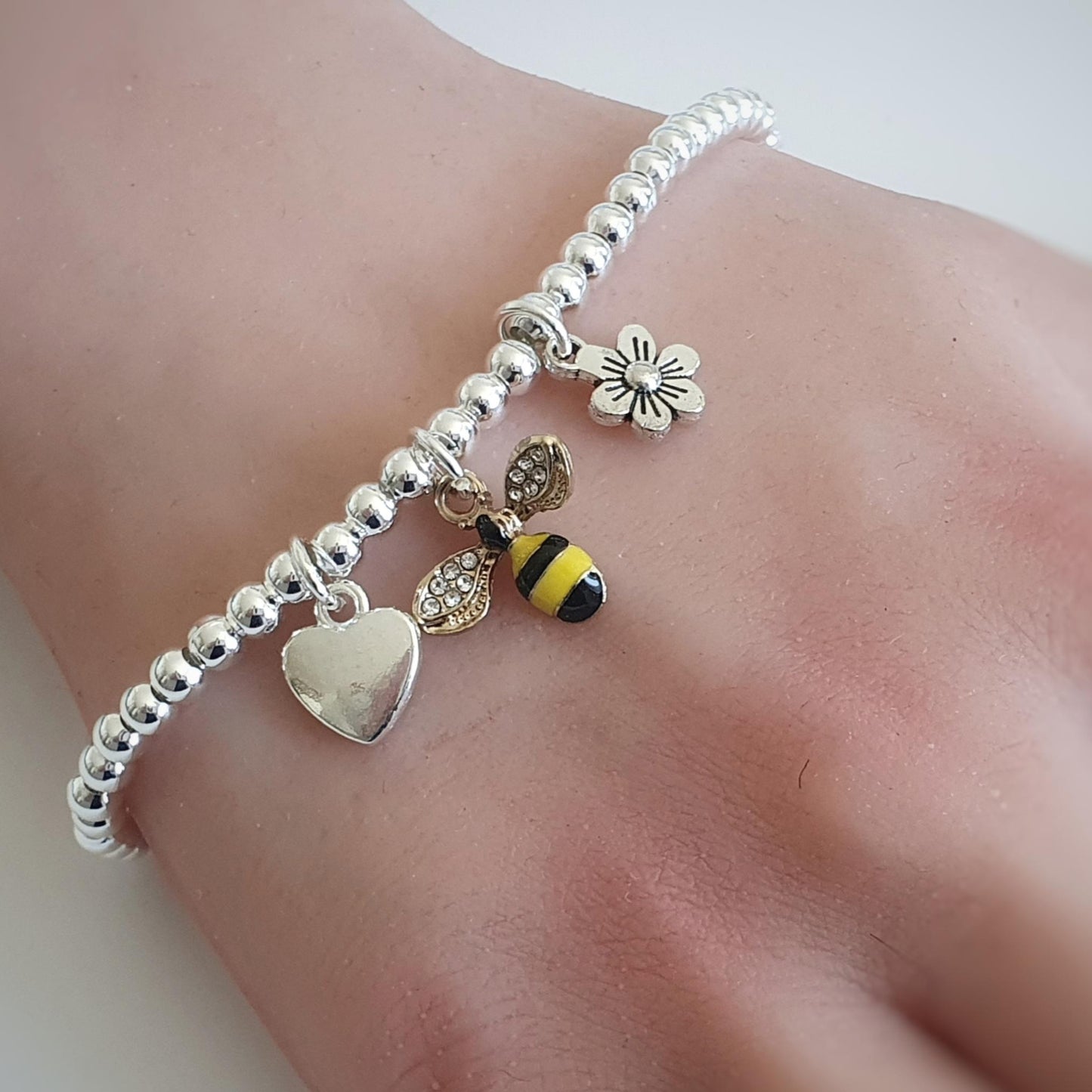 Silver bracelet with heart, bee, and flower charms on a wrist against a white background