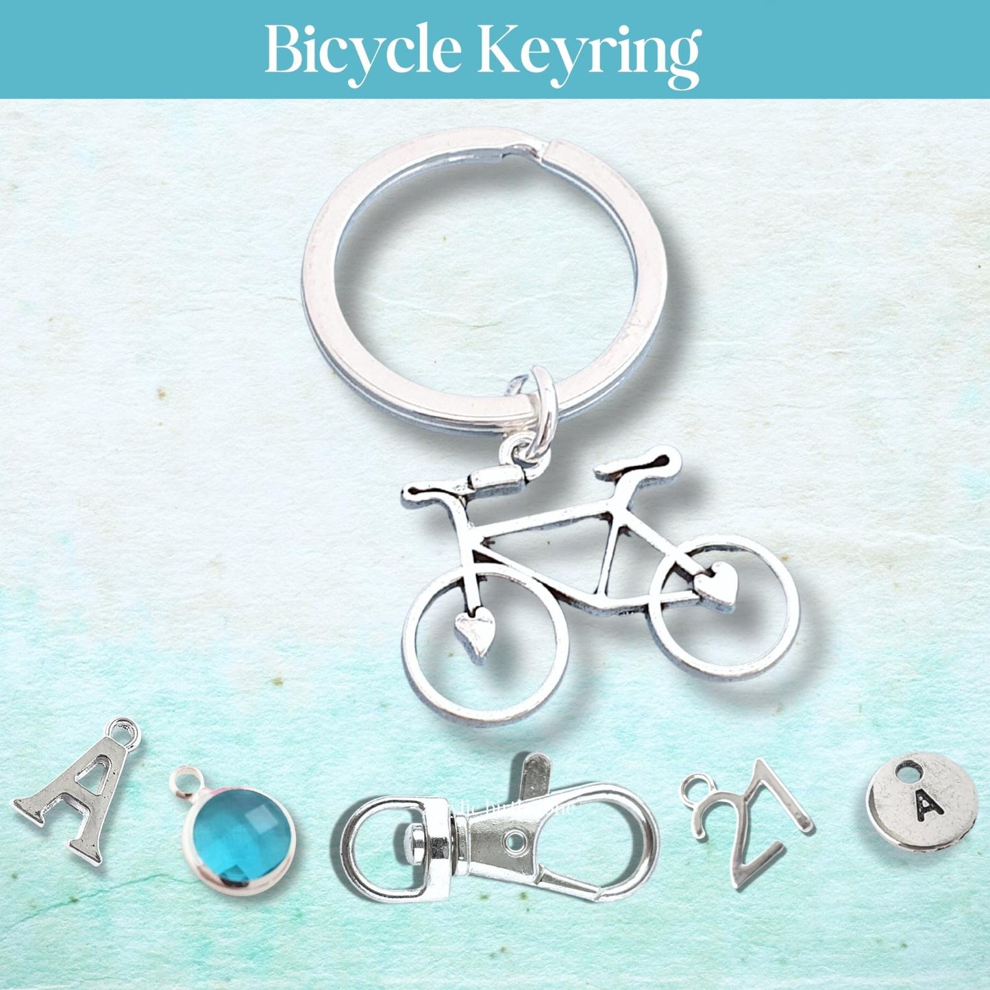 Silver bicycle keyring with additional charms on a light blue background