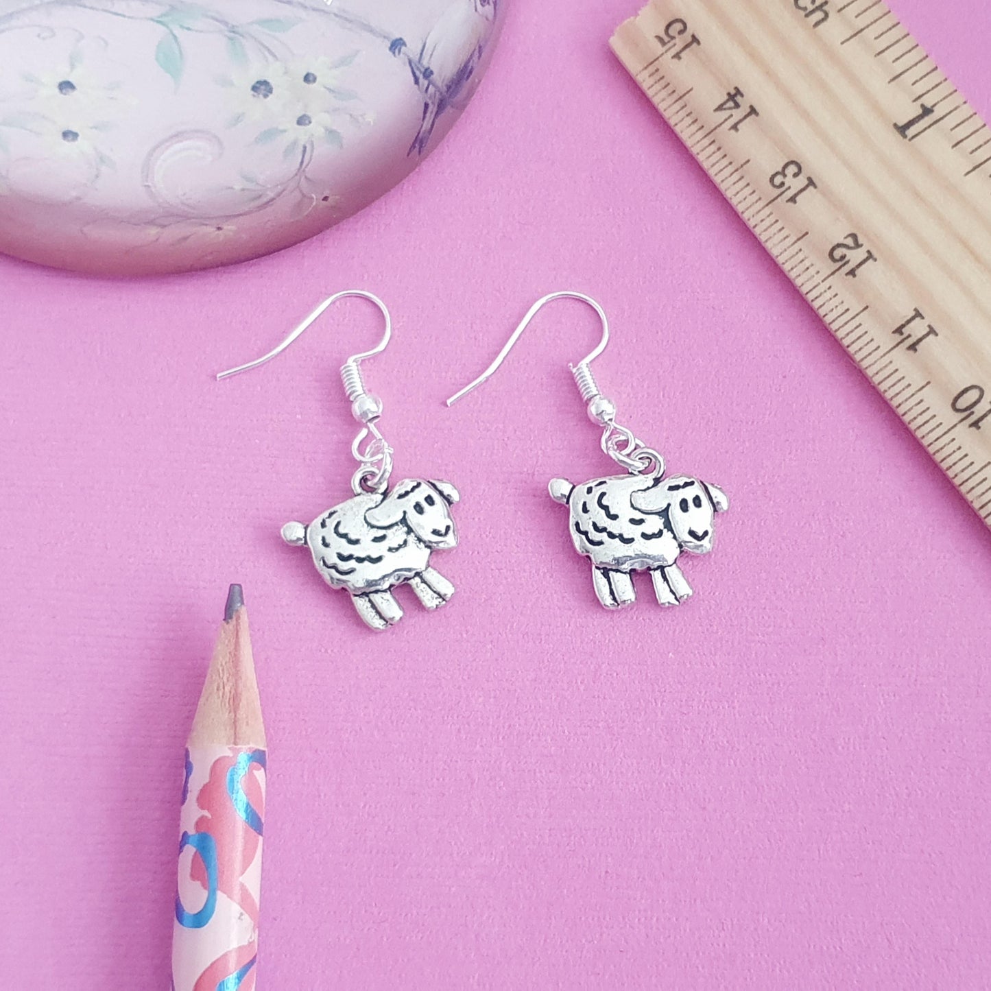 Sheep-shaped earrings on a pink background with a ruler for scale.