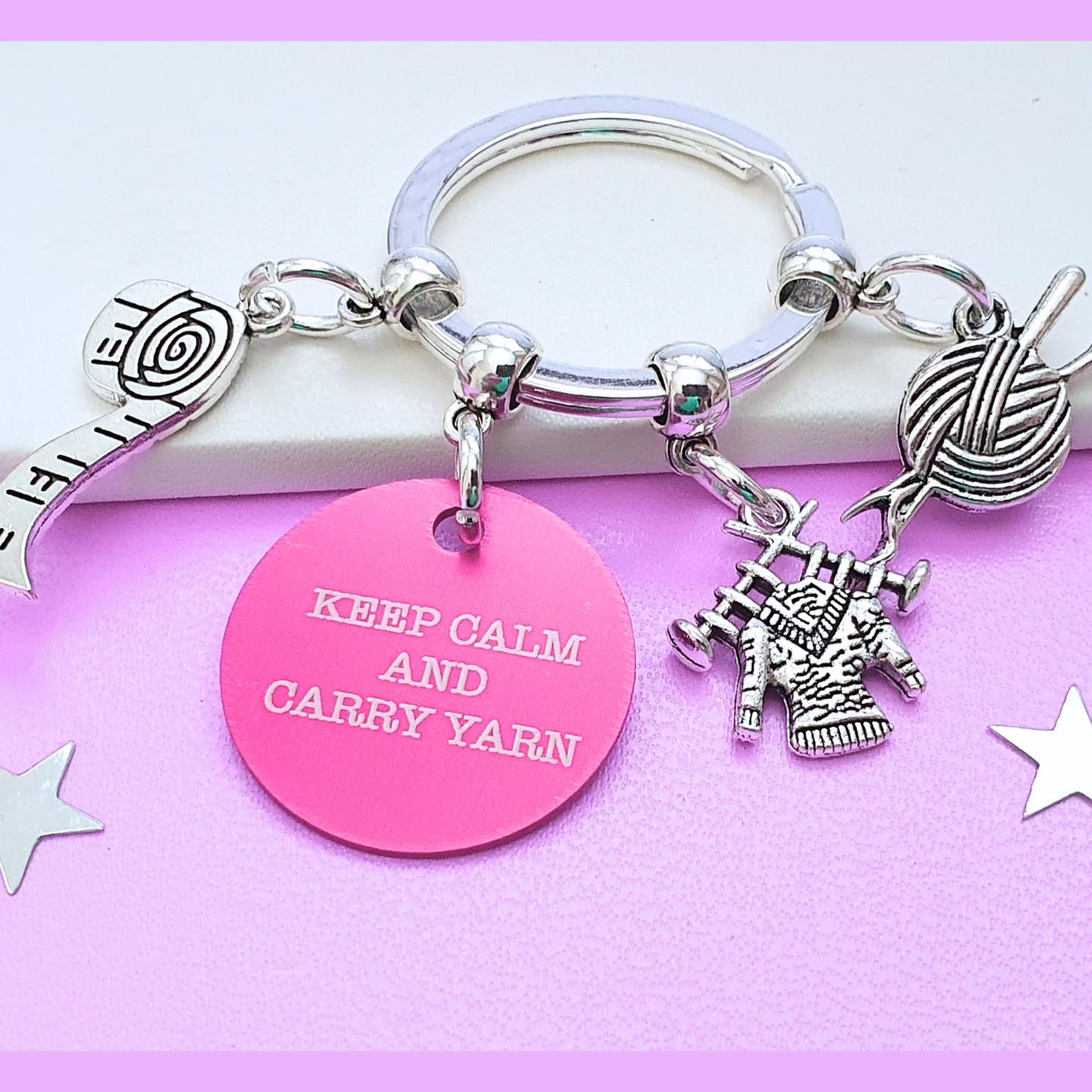 Keychain with charms including a yarn ball, knitting needles, and a pink tag with 'KEEP CALM AND CARRY YARN' text on a pink background.