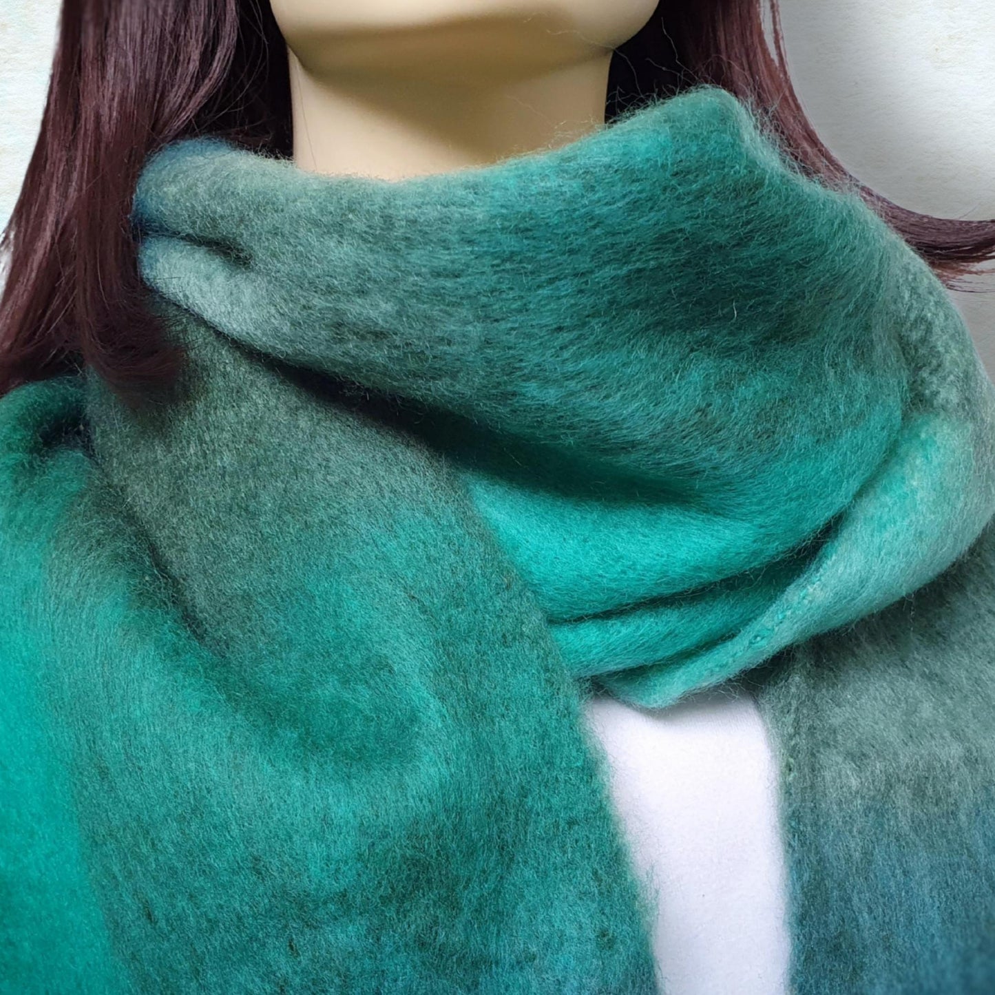 Teal green blanket scarf wrapped around a mannequin with a neutral background