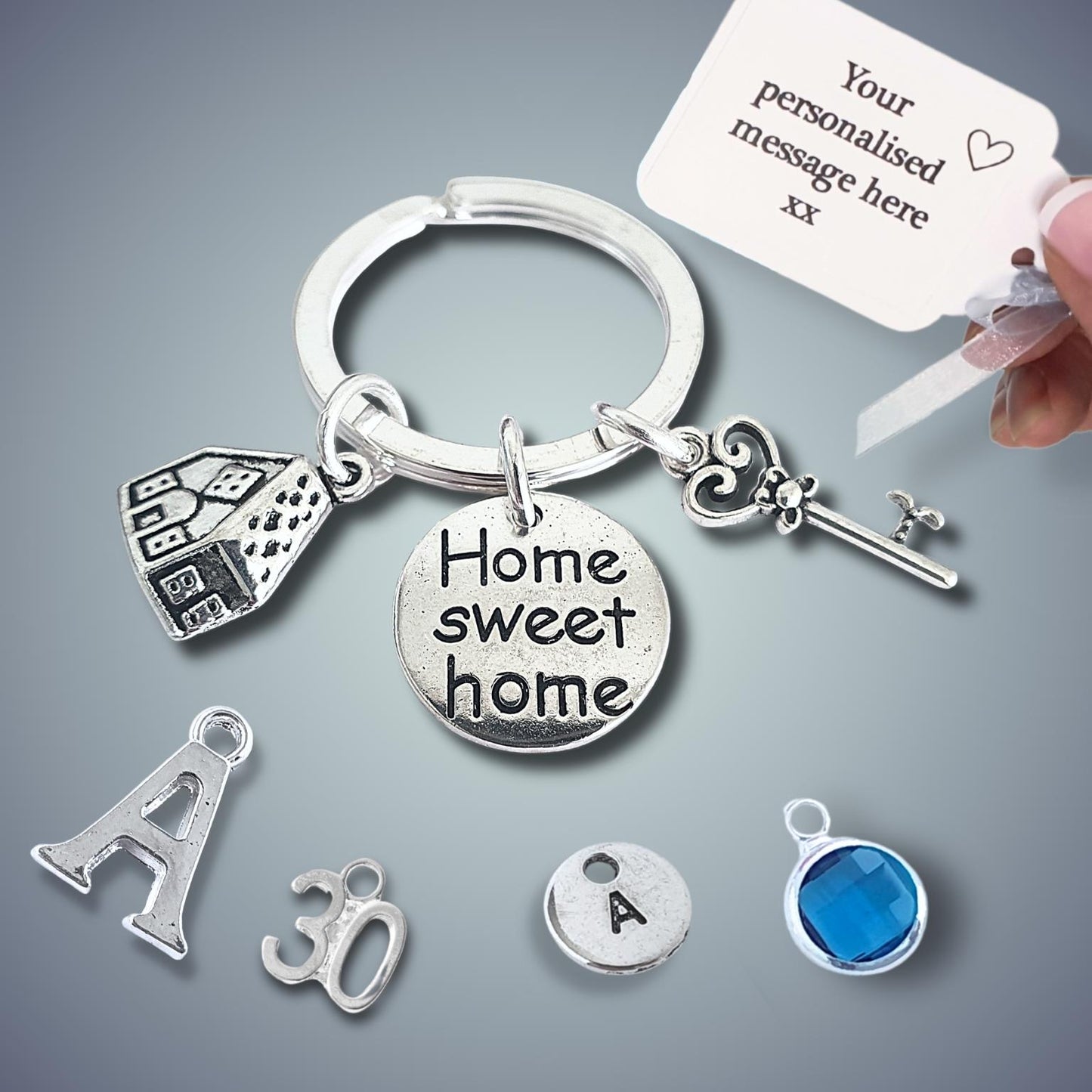 Silver keychain with 'Home sweet home' charm and other charms on a gray background