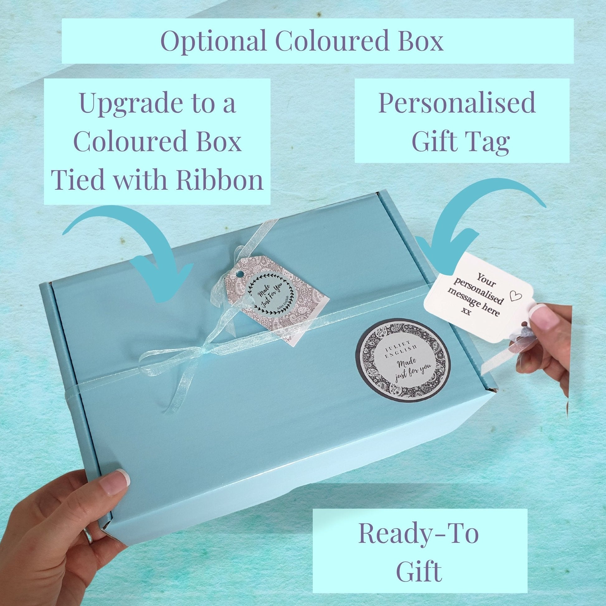 Light blue gift box with a personalised gift tag, hand holding the box against a light blue background.