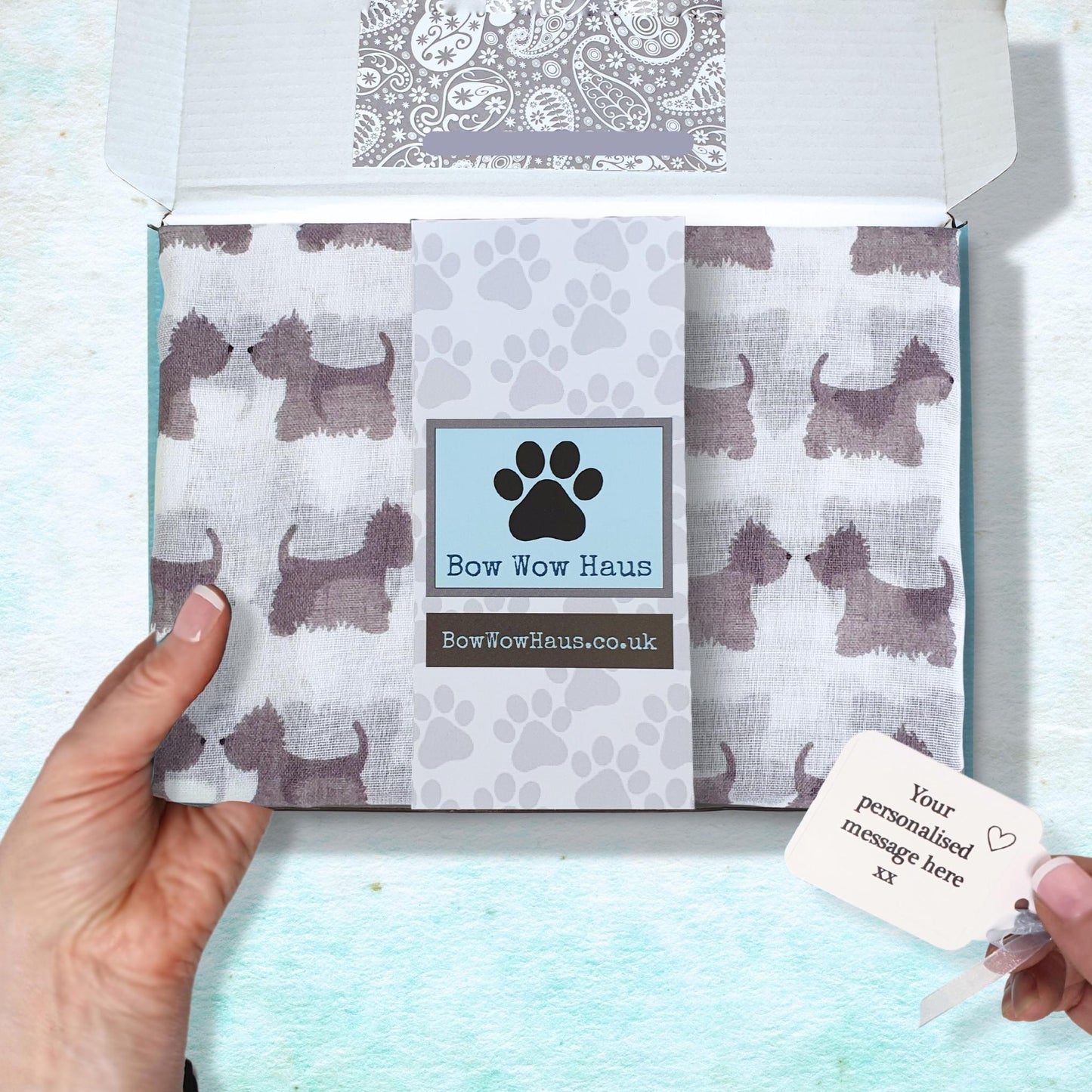 Box with a folded scotty dog print scarf and personalized message card, held by a hand against a light blue background.