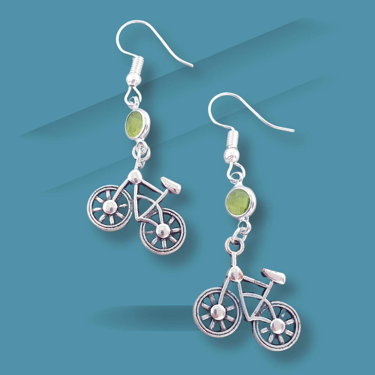 Bicycle-shaped earrings with green gemstones on a blue background