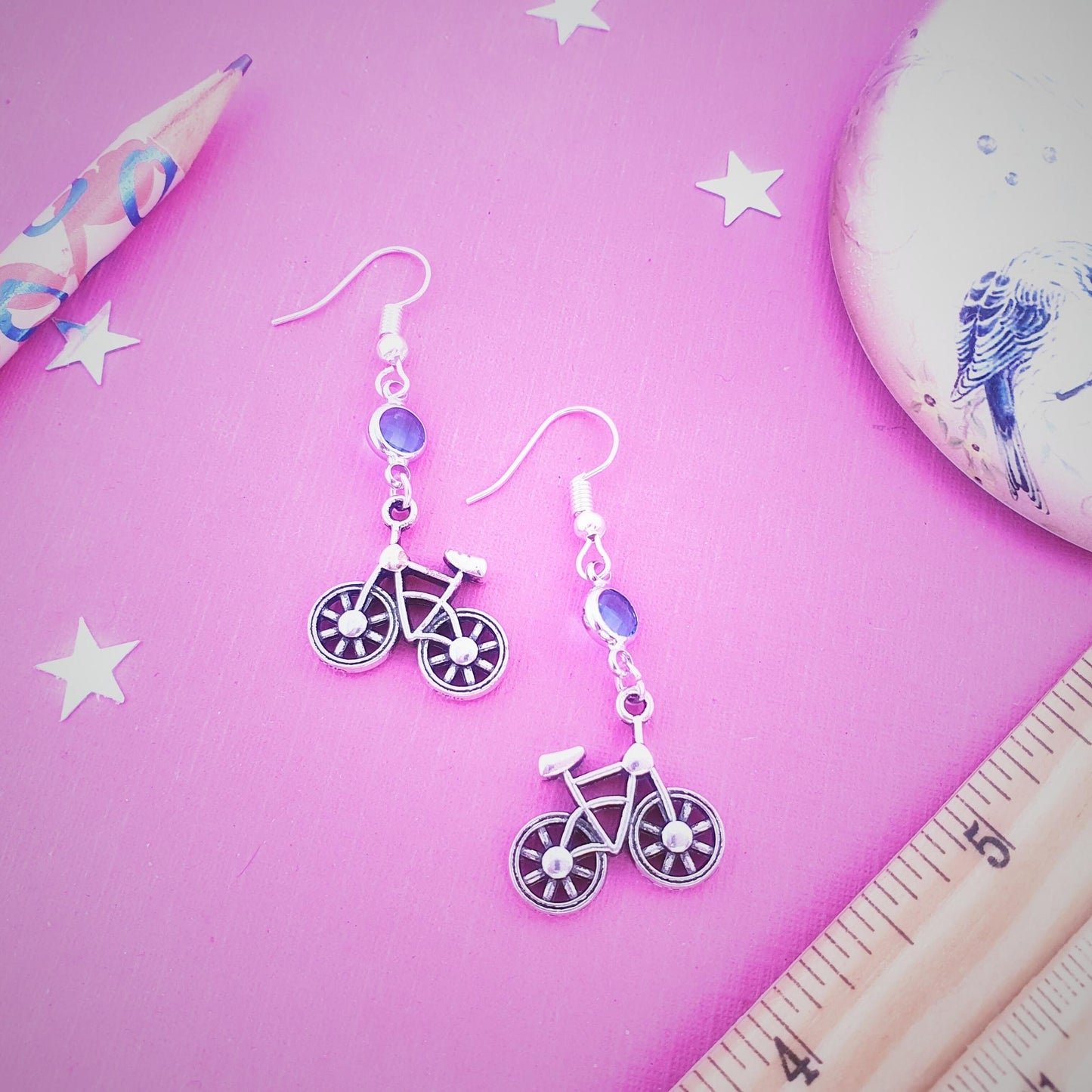 Bicycle-shaped earrings on a pink surface with a ruler and pencil.