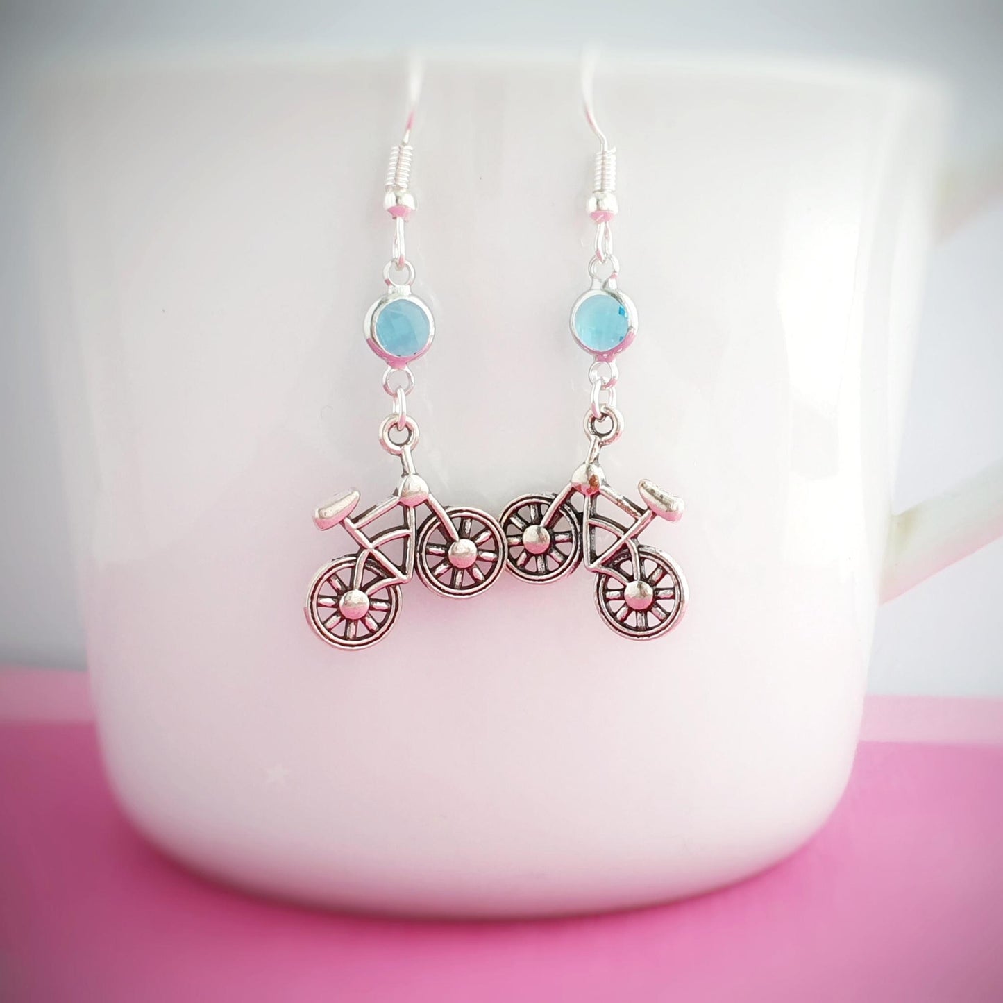 Bicycle-shaped earrings with blue birthstone charms on a white mug.