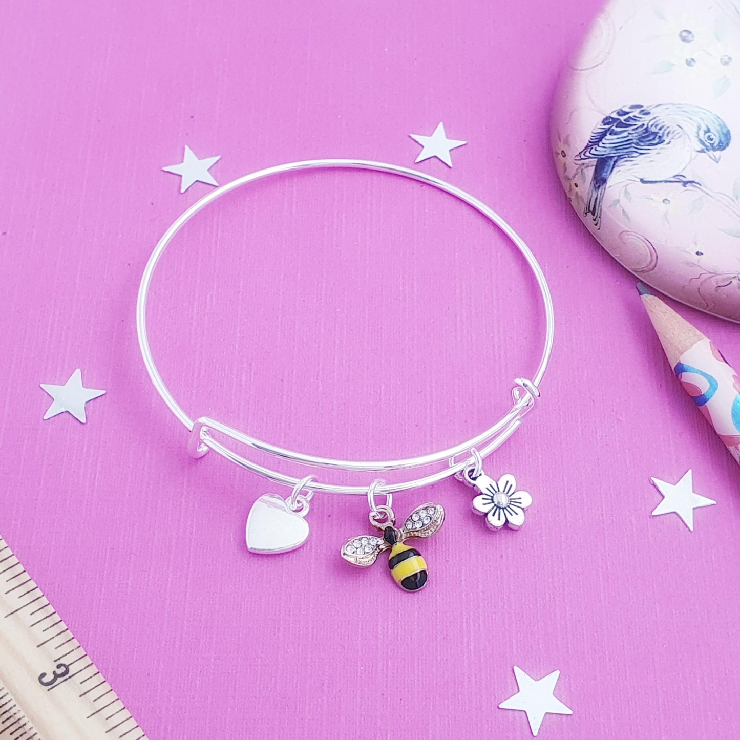 Silver bracelet with charms on a pink background with stars and a ruler.