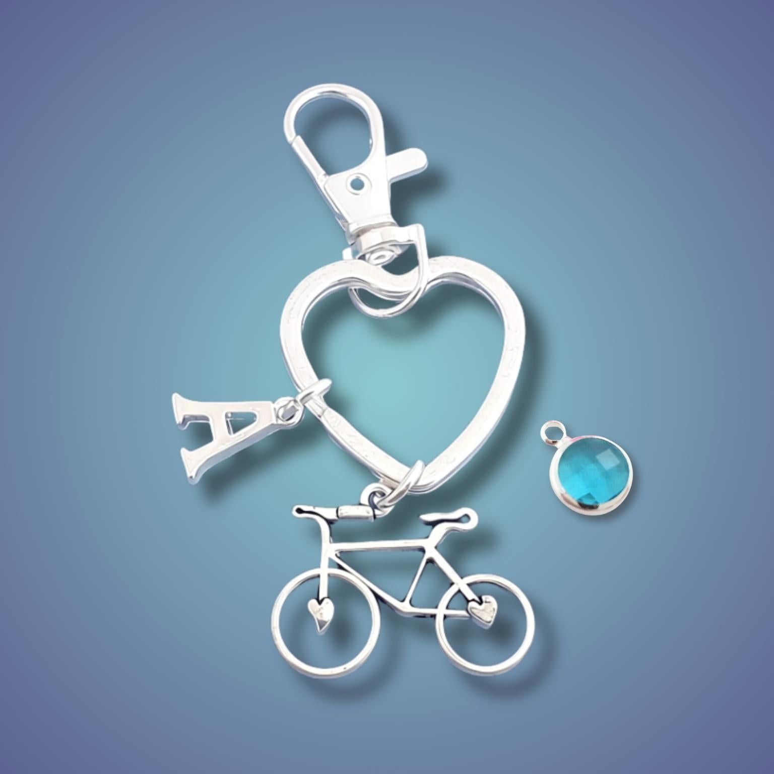 heart shaped keyring with a bicycle charm and a bag clasp on a blue gradient background