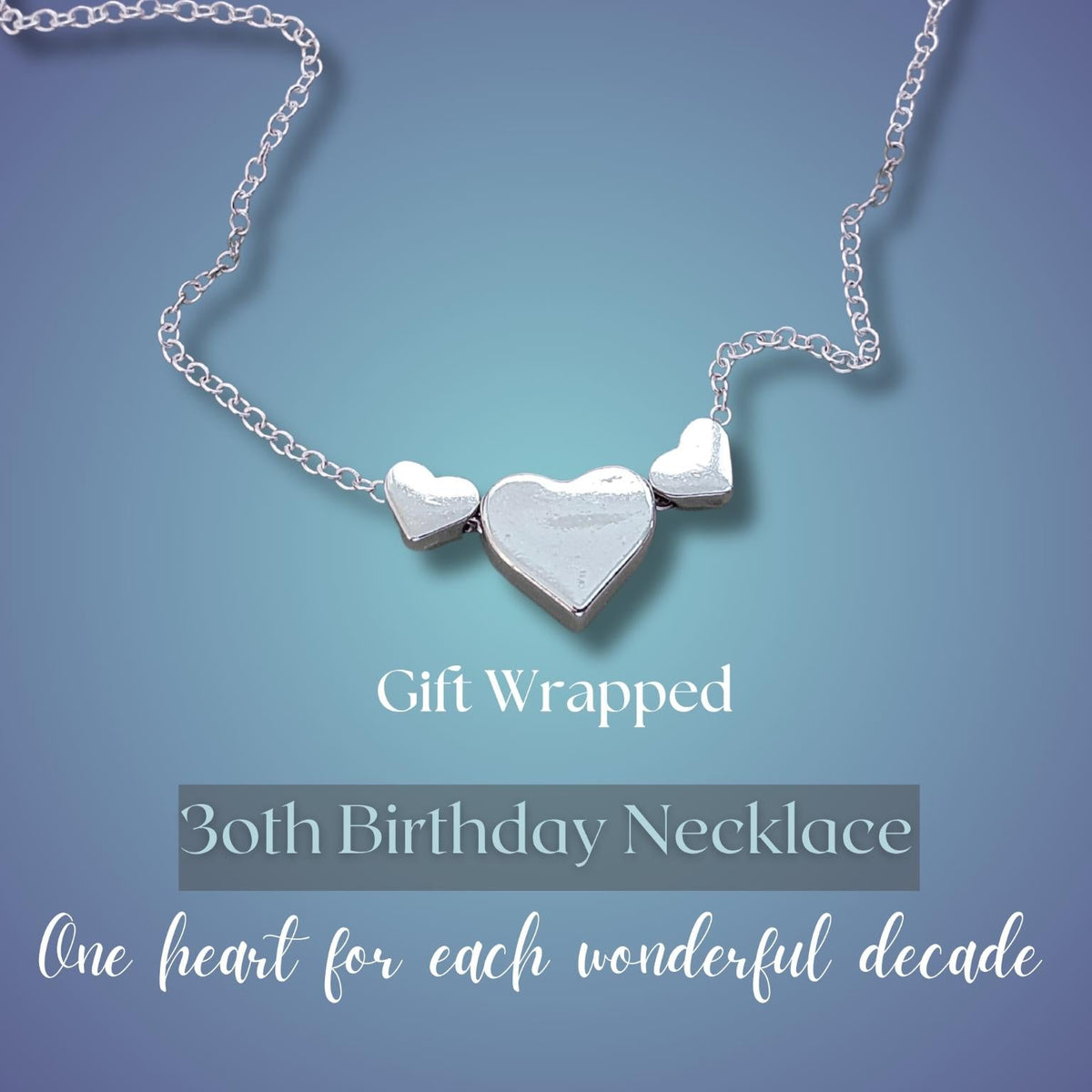 A silver necklace with three heart-shaped pendants 2 small and one large size, displayed on a blue gradient background with text reading 'Gift Wrapped 30th Birthday Necklace One heart for each wonderful decade'.