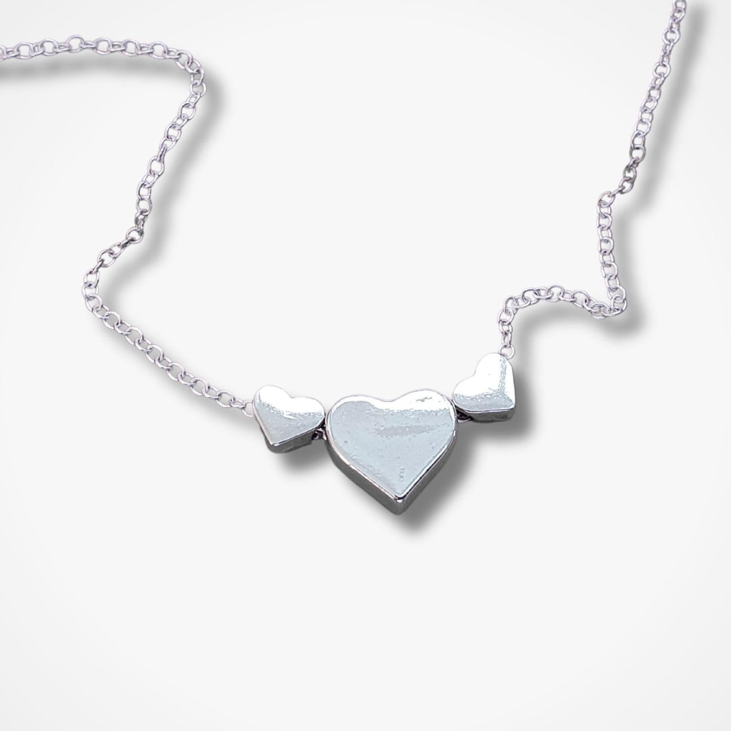 A silver heart necklace featuring three heart pendants on a delicate chain, displayed against a clean white background.