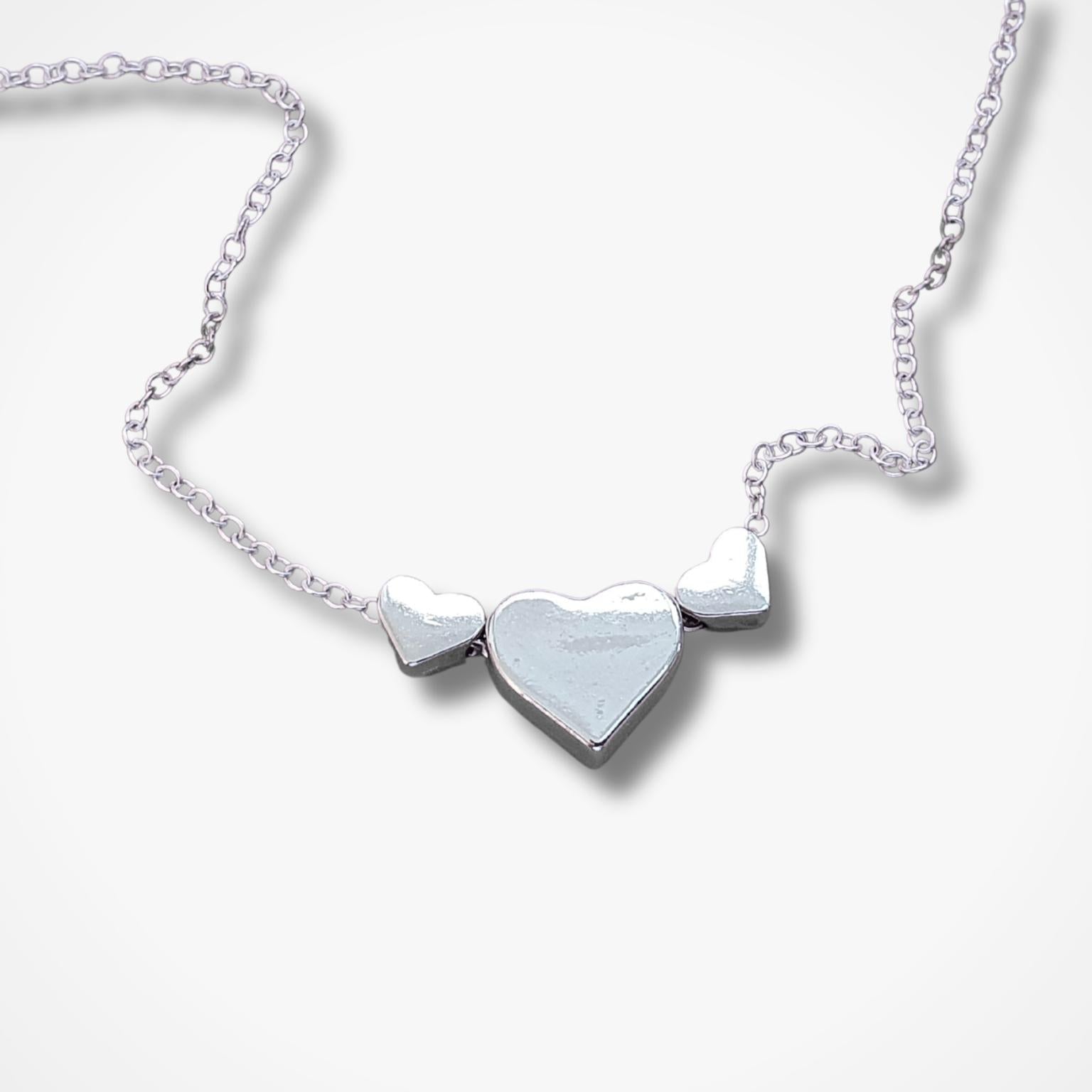 A silver heart necklace featuring three heart pendants on a delicate chain, displayed against a clean white background.