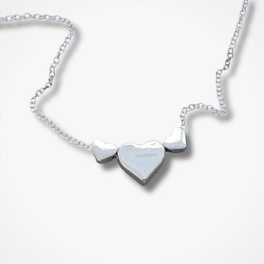 A silver heart necklace featuring three heart pendants on a delicate chain, displayed against a clean white background.