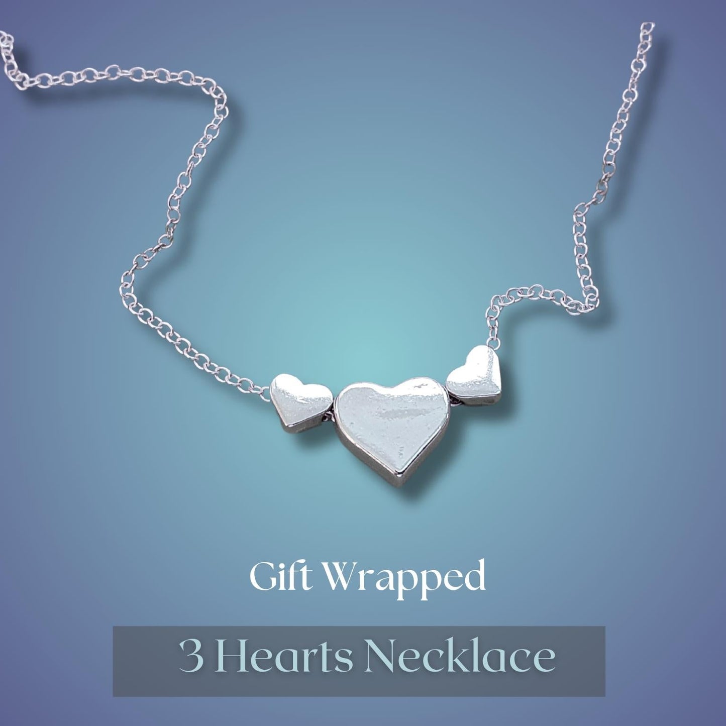 A silver 3-heart necklace with a centre heart and side hearts, displayed on a blue gradient background with 'Gift Wrapped 3 Hearts Necklace' text below.