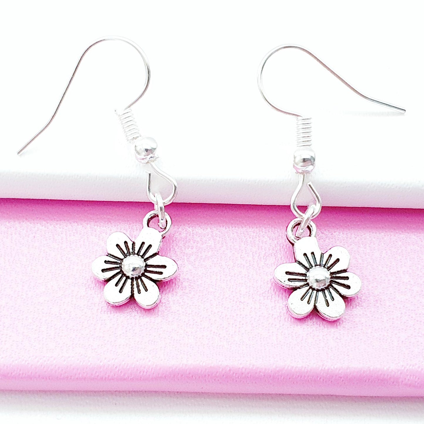 Silver flower-shaped earrings on a pink and white background