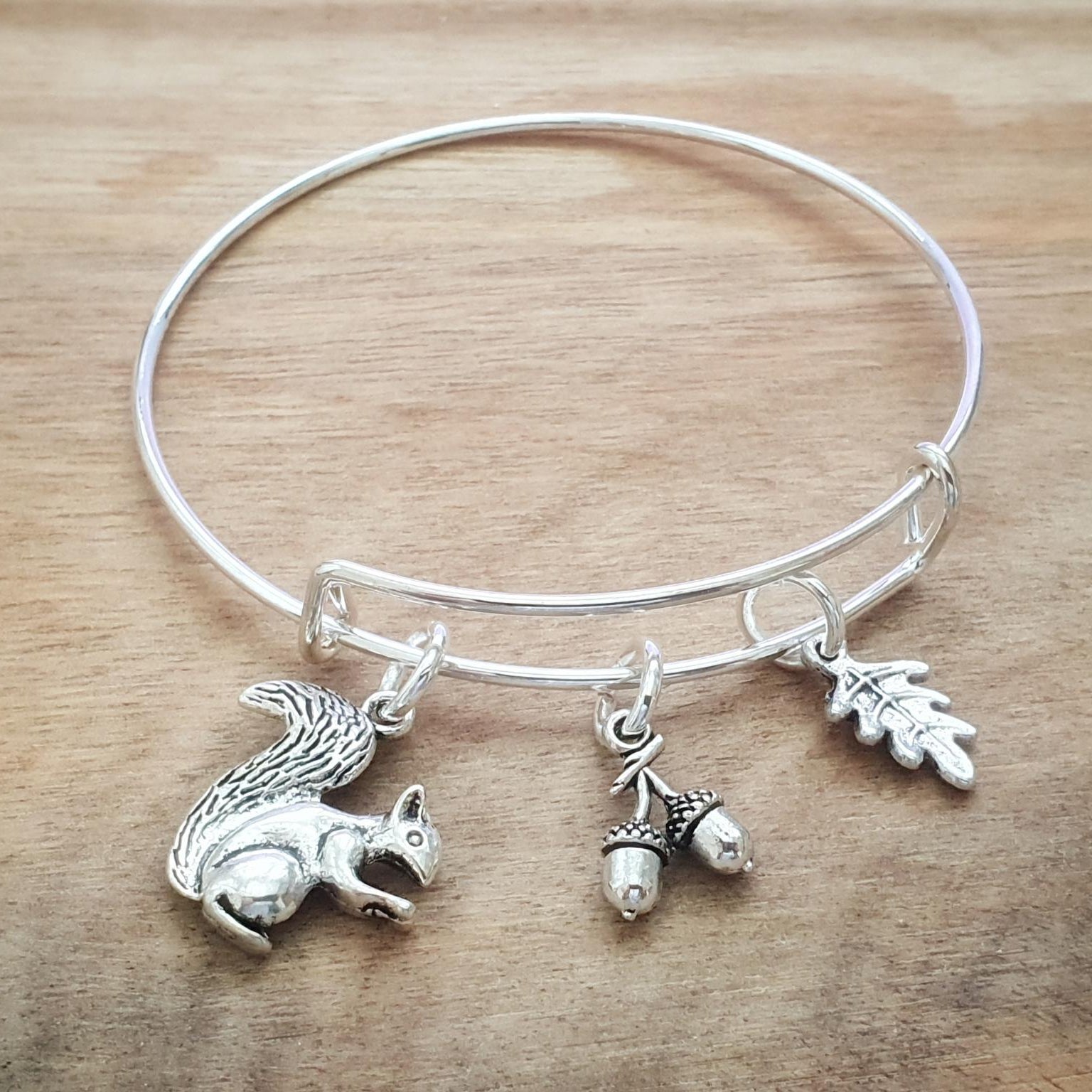 Silver adjustable bracelet with squirrel, acorn, and leaf charms on a wooden surface
