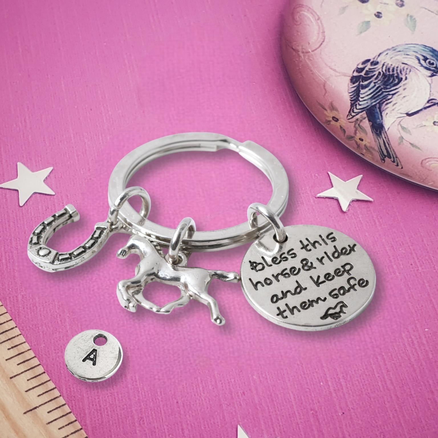 Silver keychain with horse charm and engraved text on a pink surface with decorative elements.