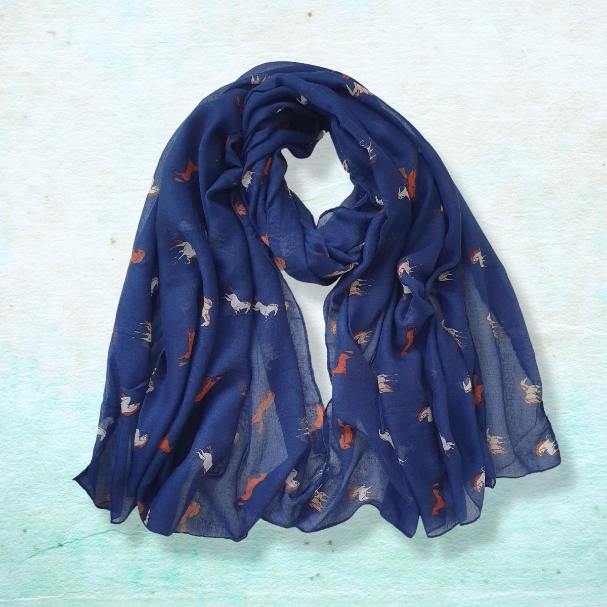 A lightweight navy blue scarf with a delicate pattern of small white and orange horses, draped on a textured light blue background.