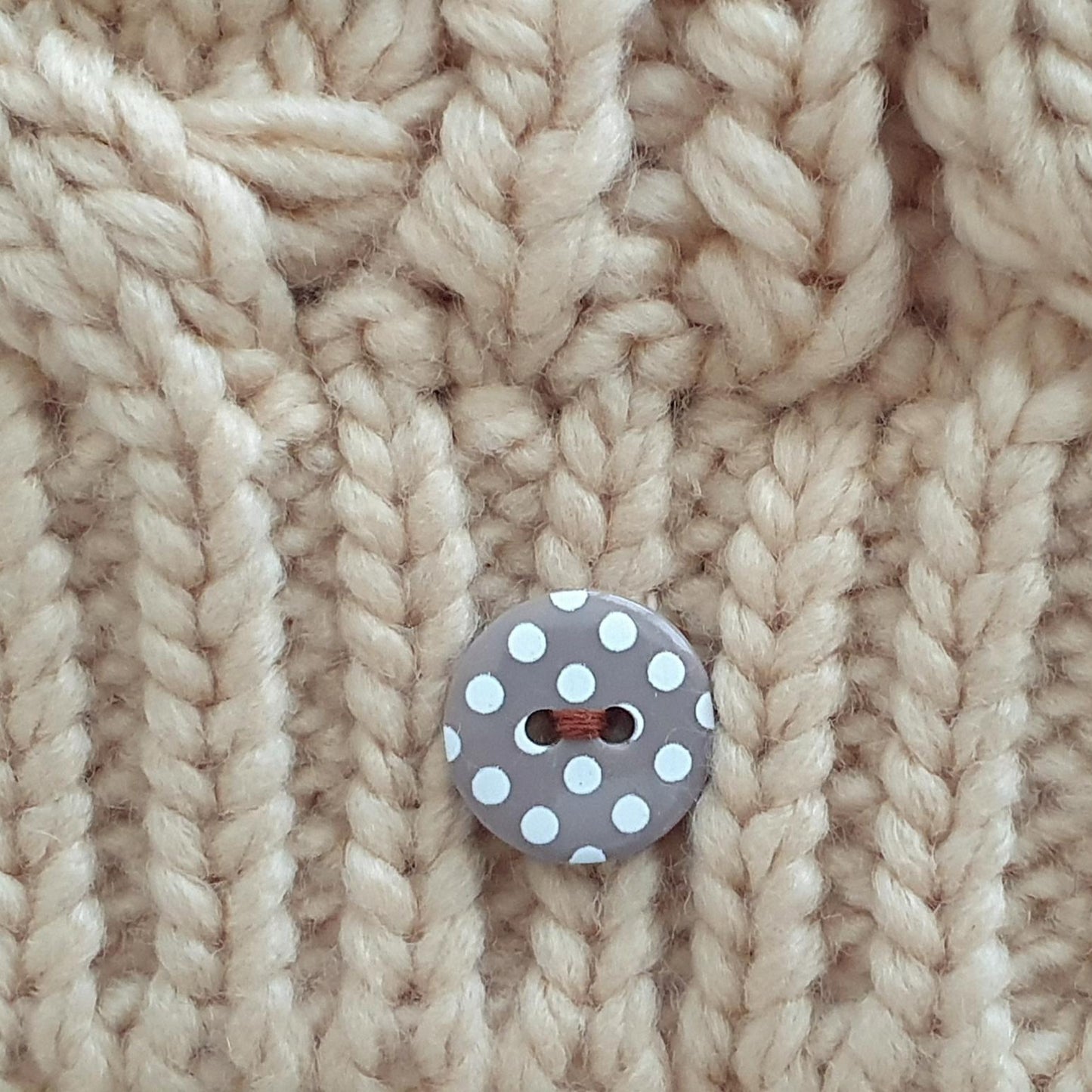 Close-up of a chunky cream-colored cable-knit fabric with a single gray button featuring white polka dots.