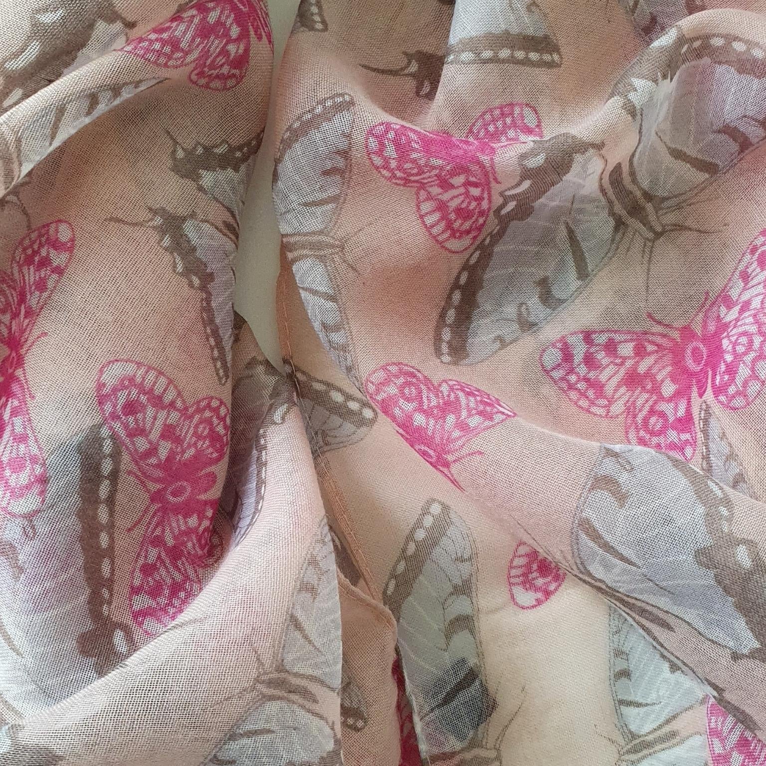 A close-up of sheer pink fabric with a printed butterfly pattern in pink, grey blue, and brown, draped in soft folds.