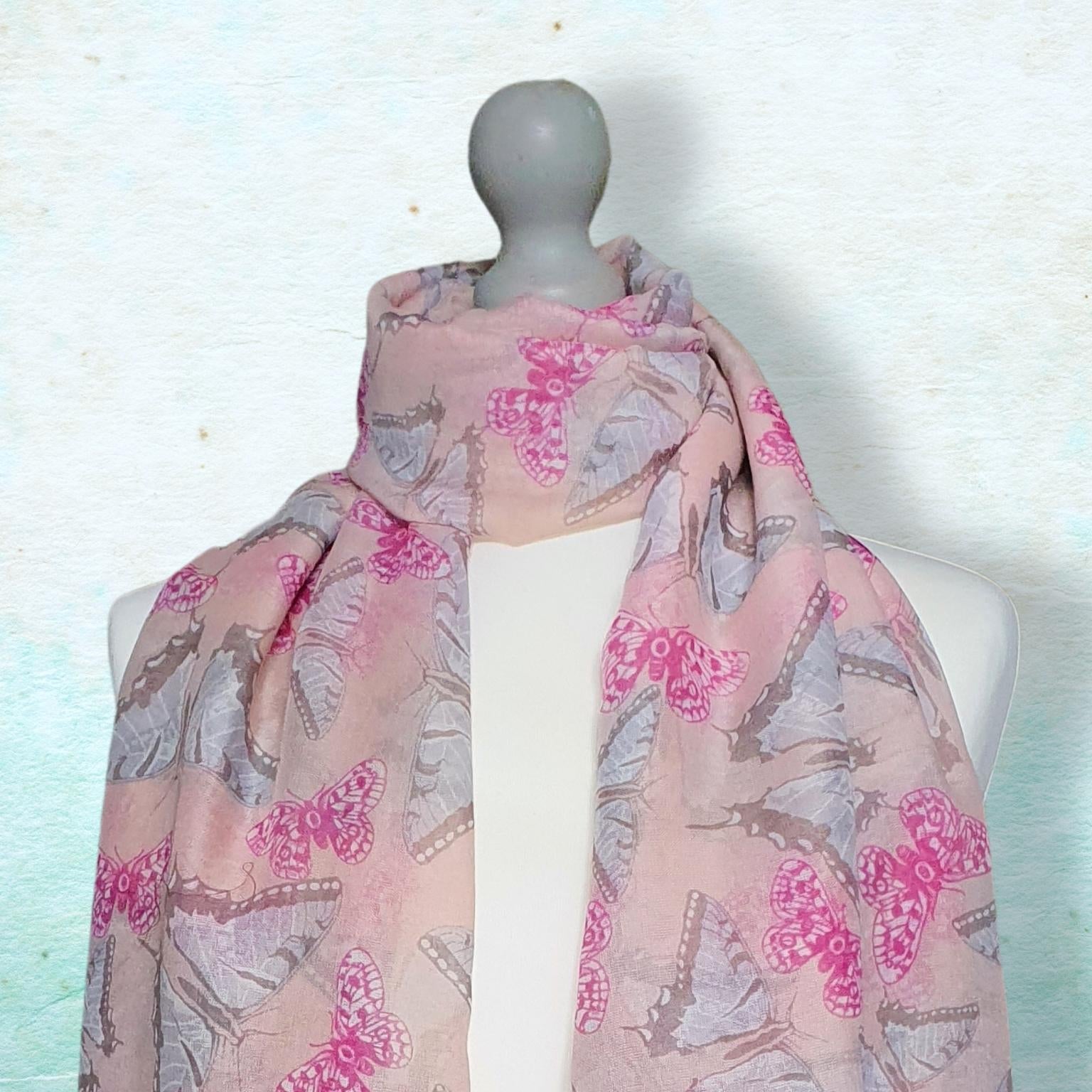 A lightweight pink scarf with a butterfly print draped on a white mannequin torso against a textured light blue background.