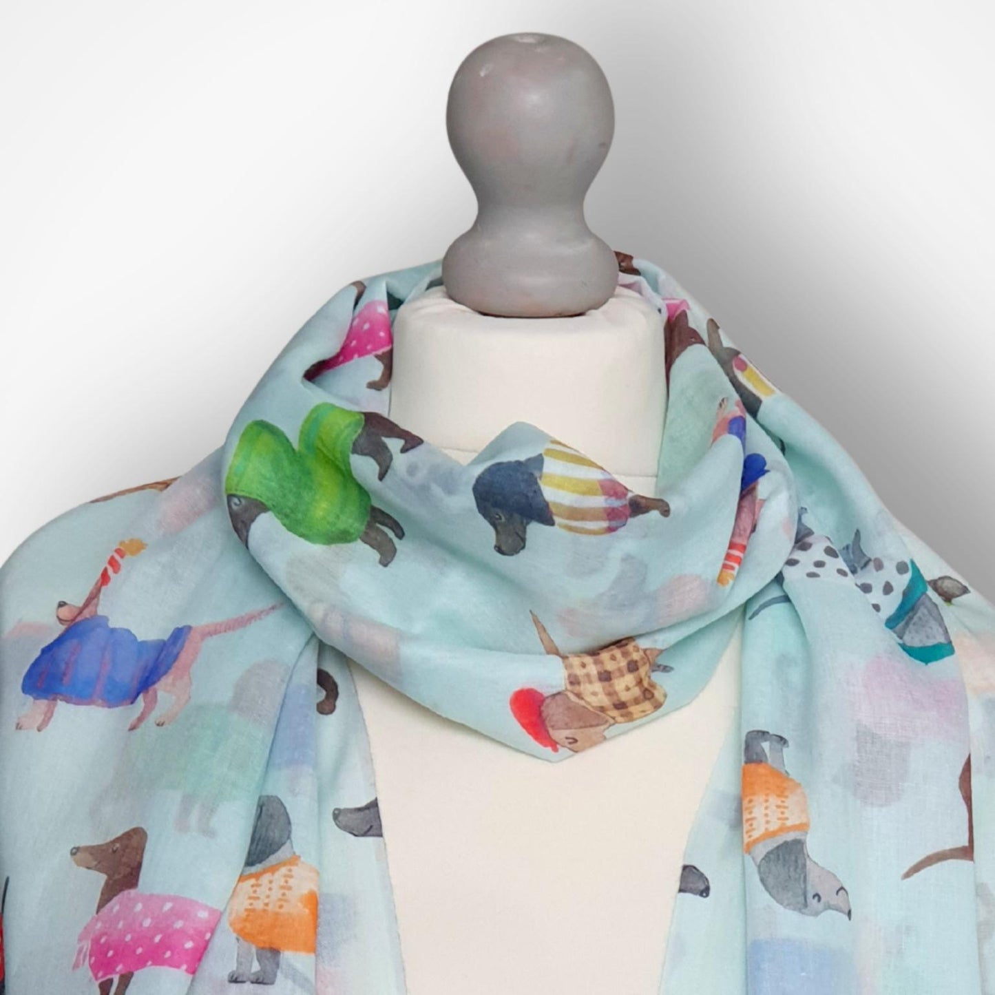Mannequin wearing a colorful scarf with cartoon-like dachshund illustrations on a light gray background