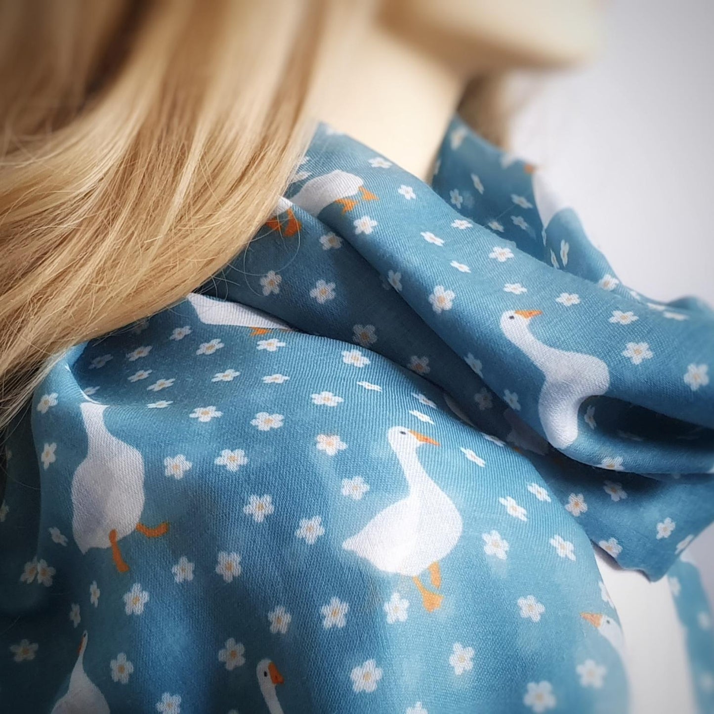 Close-up of a blue fabric with white floral and goose patterns, worn by a person with long blonde hair.