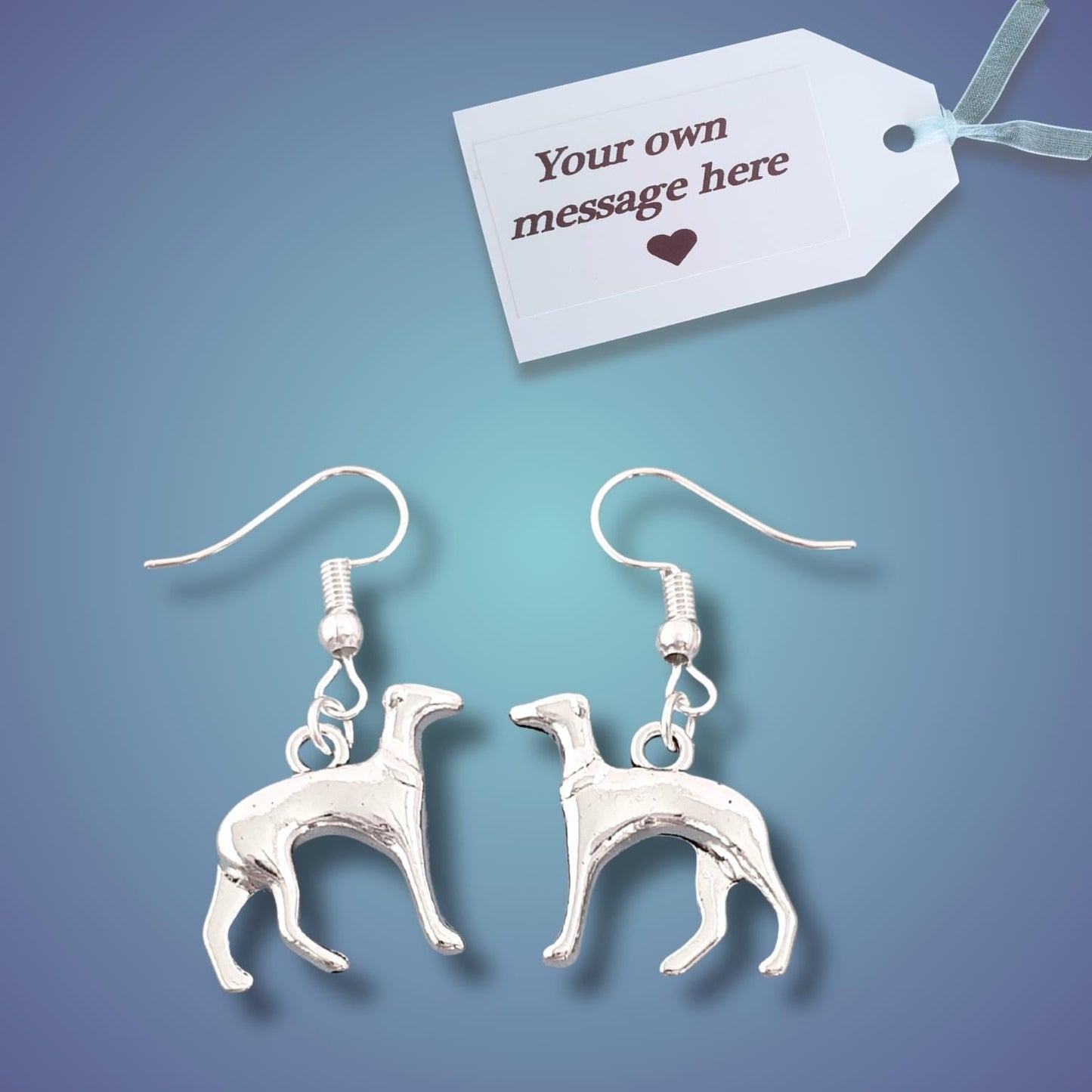 A pair of silver dangle earrings shaped like greyhounds, displayed on a blue gradient background with a white gift tag that reads 'Your own message here'.
