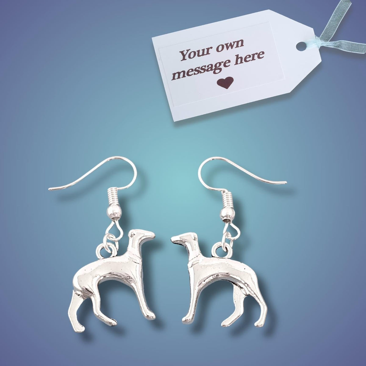 A pair of silver dangle earrings shaped like greyhounds, displayed on a blue gradient background with a white gift tag that reads 'Your own message here'.