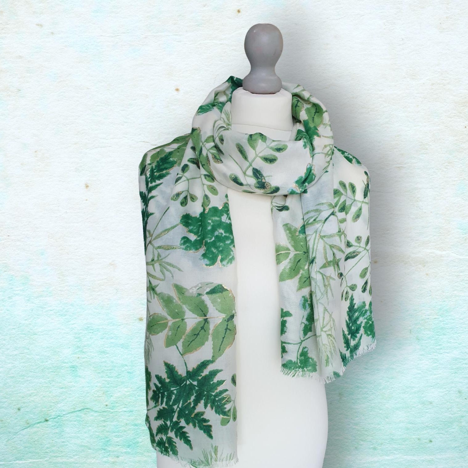 Mannequin wearing a green leaf-patterned scarf on a light blue background