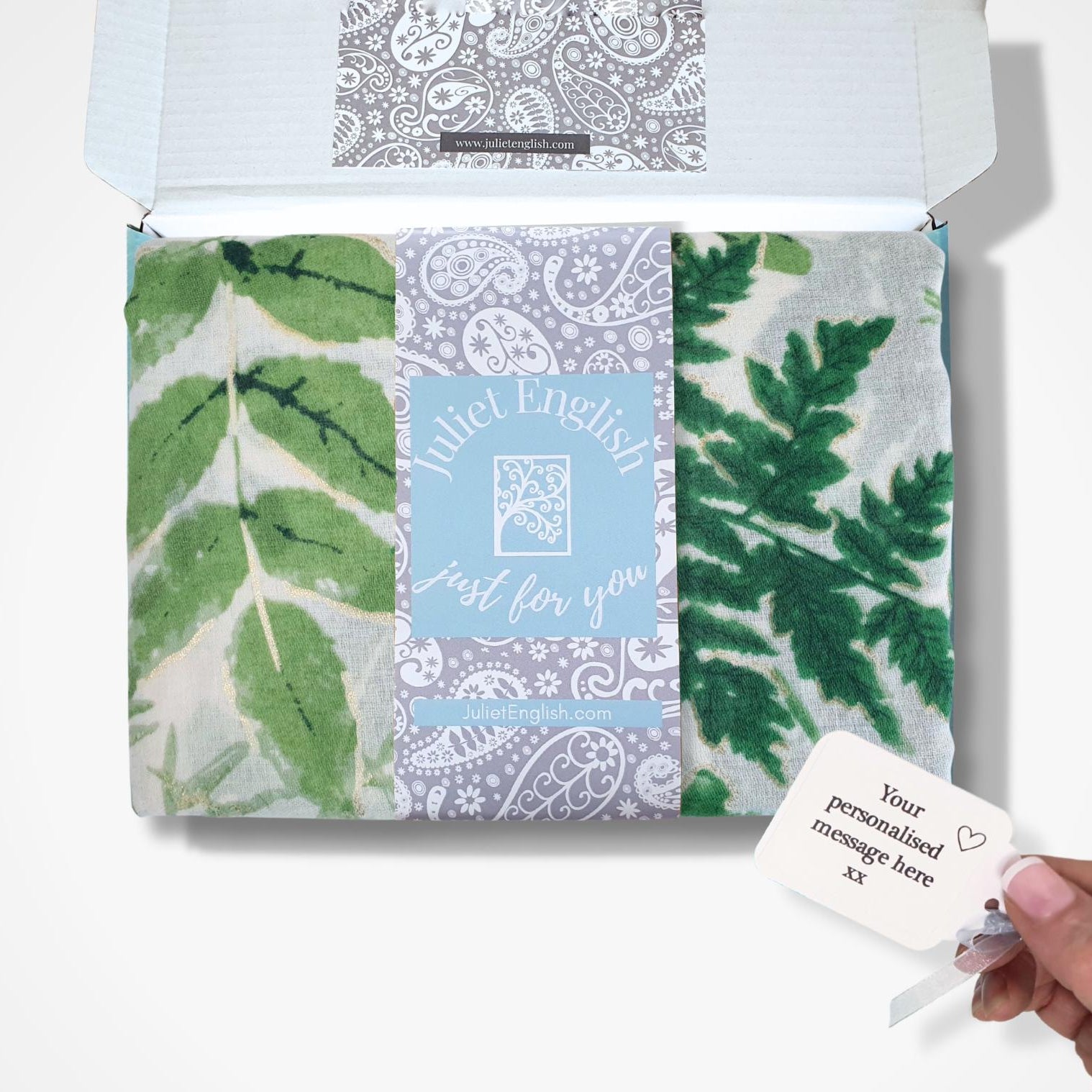 Packaged scarf with leaf patterns and a personalised card on a white background