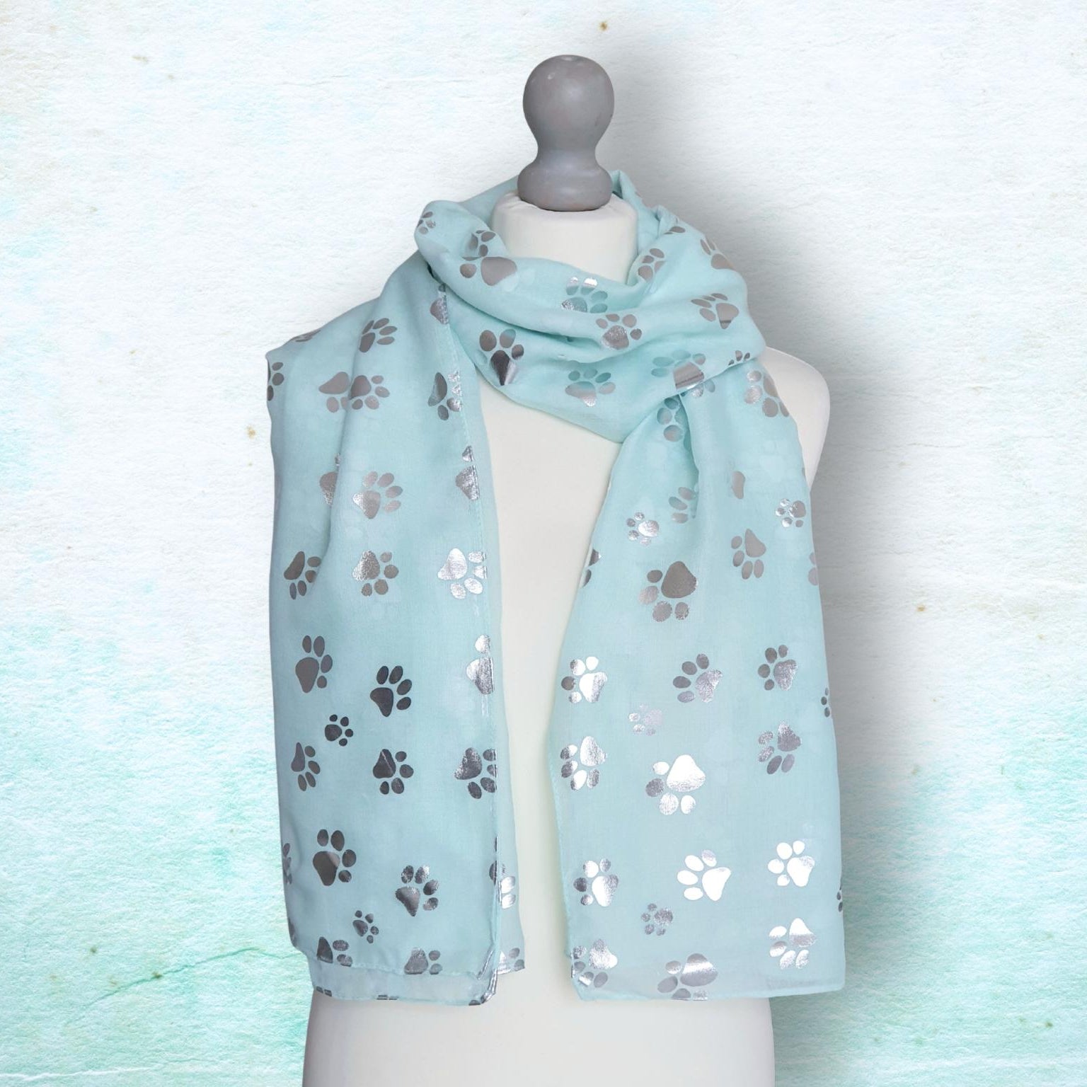 Light aqua scarf with paw print pattern on a mannequin against a light blue background