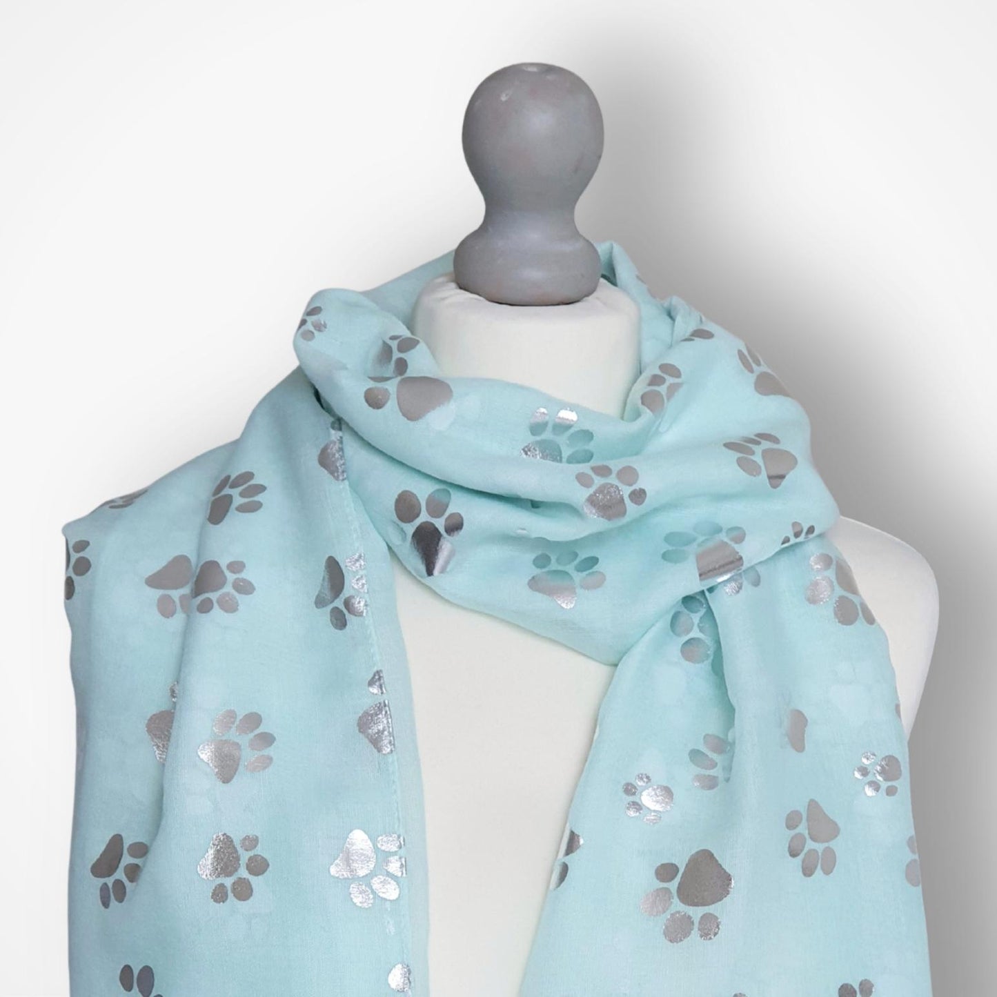 Light aqua scarf with paw print pattern on a mannequin against a white background