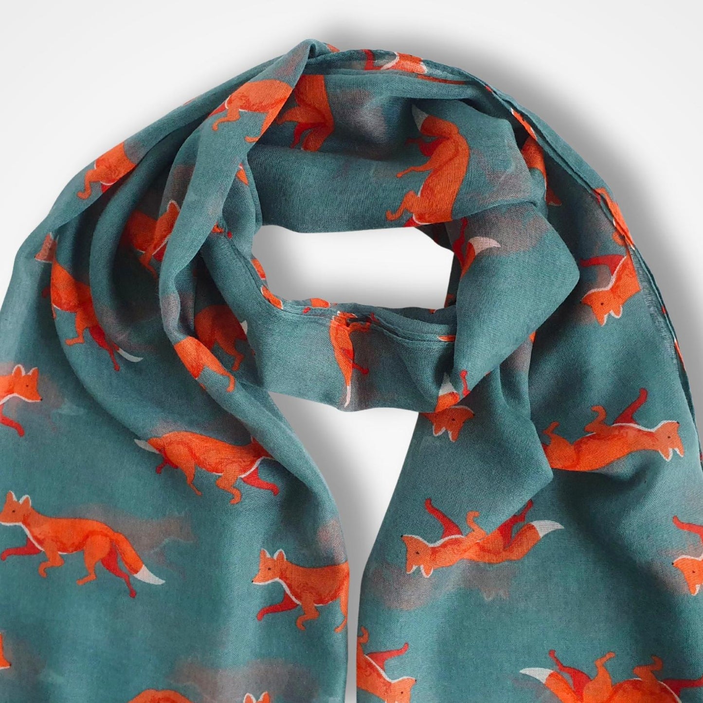 A teal green scarf with a repeating pattern of orange foxes, draped to show its soft texture and print against a light gray background.