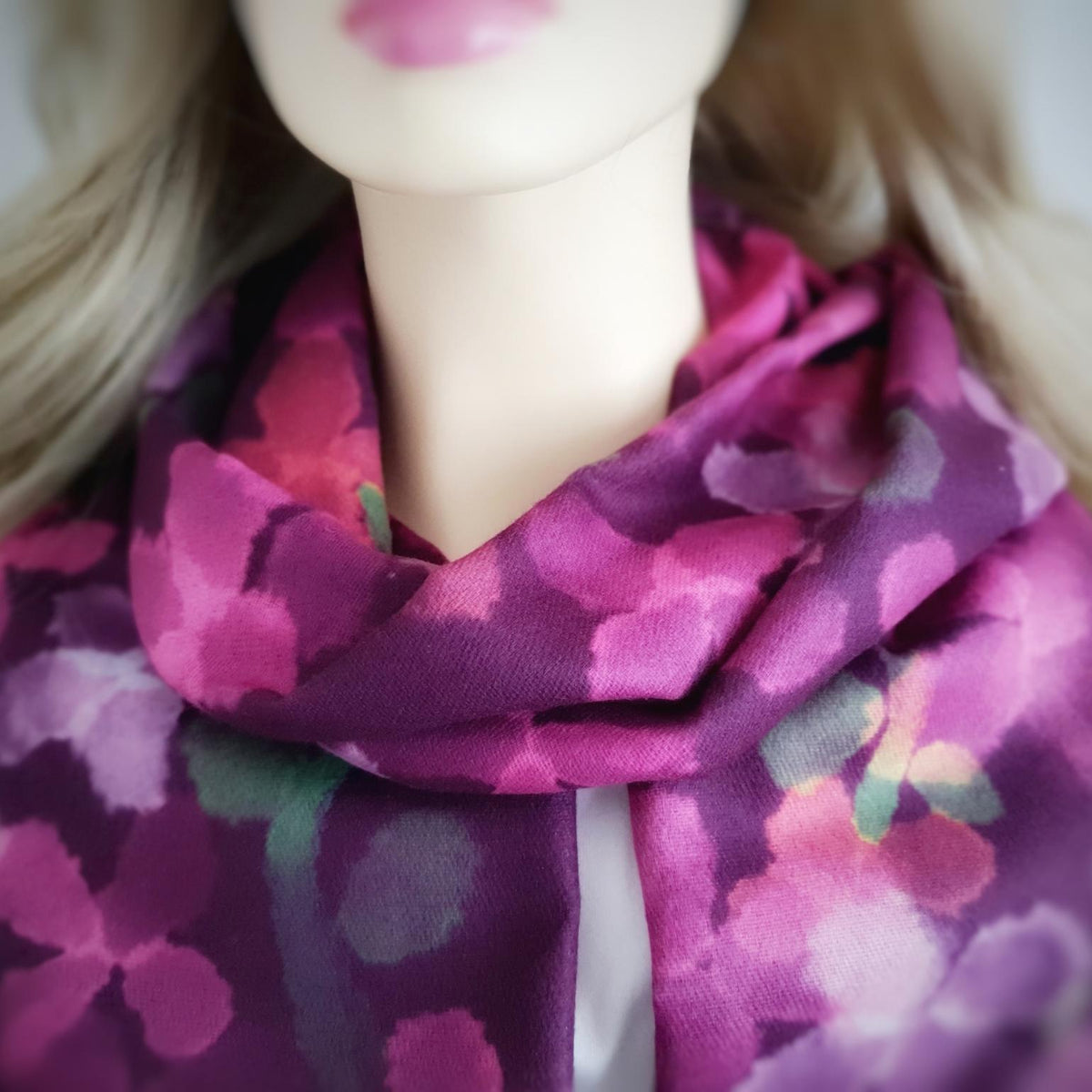 A close-up of a floral scarf in shades of magenta, purple, and pink, styled on a blonde mannequin.