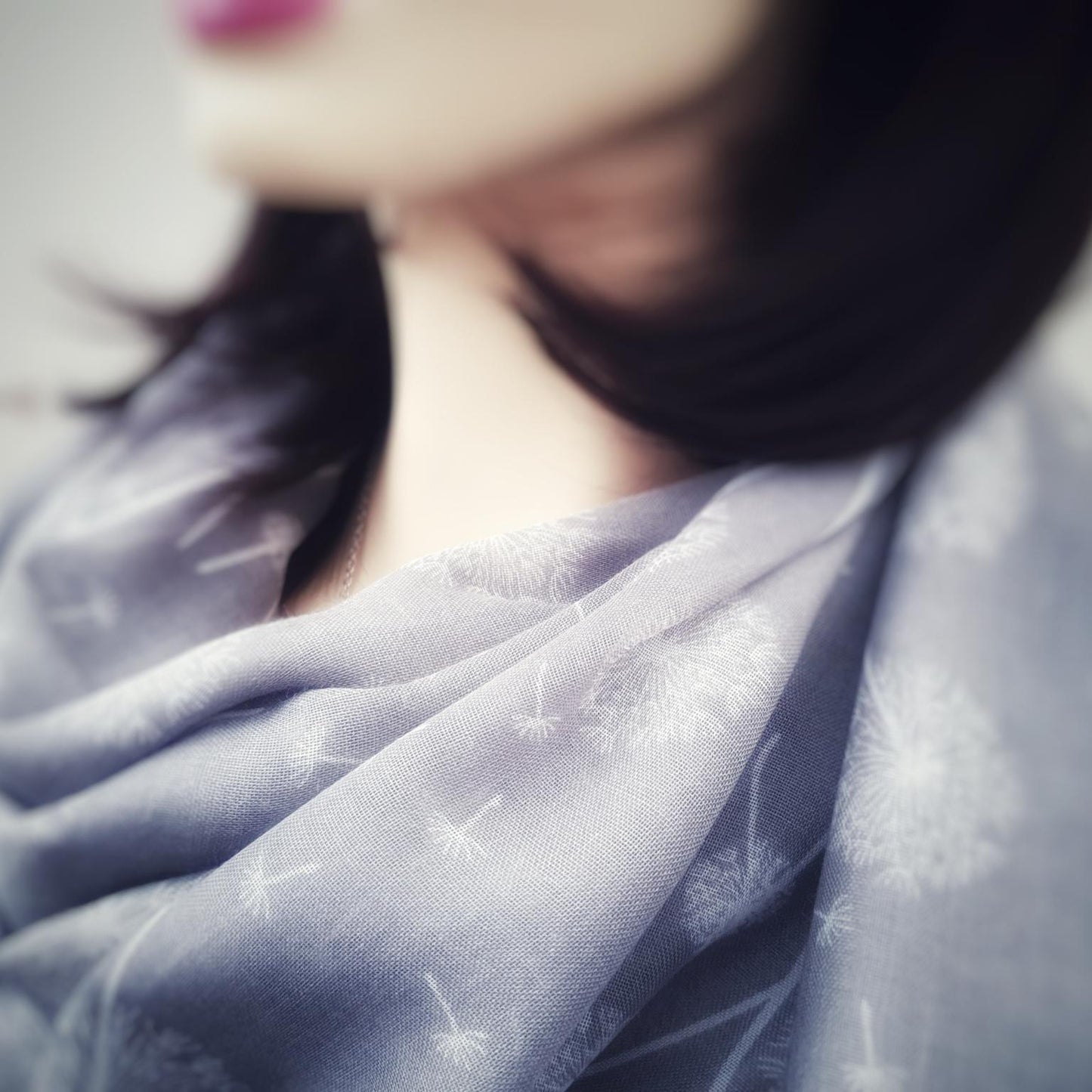 Close-up of a person wearing a grey dandelion scarf with a blurred background