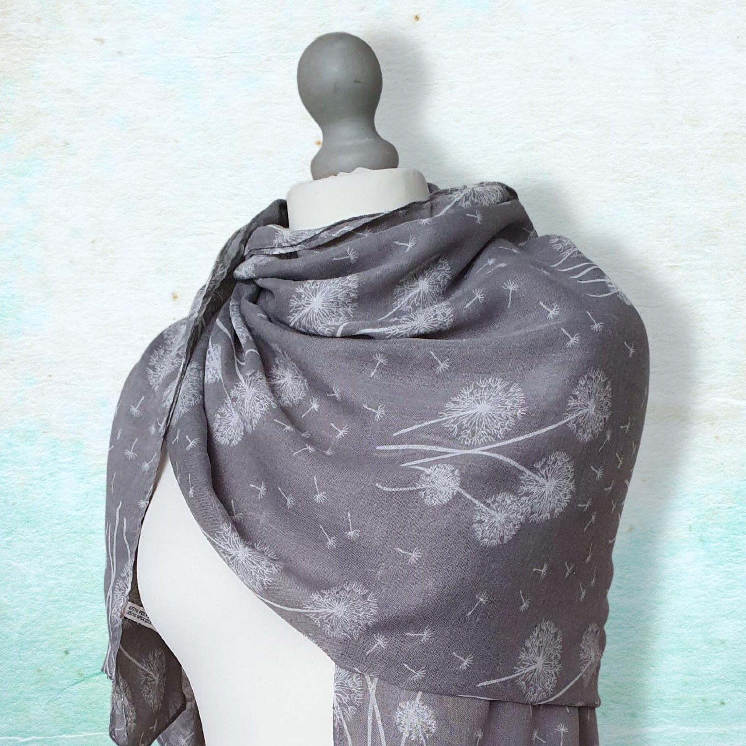 Gray scarf with dandelion pattern draped over a mannequin against a light blue background