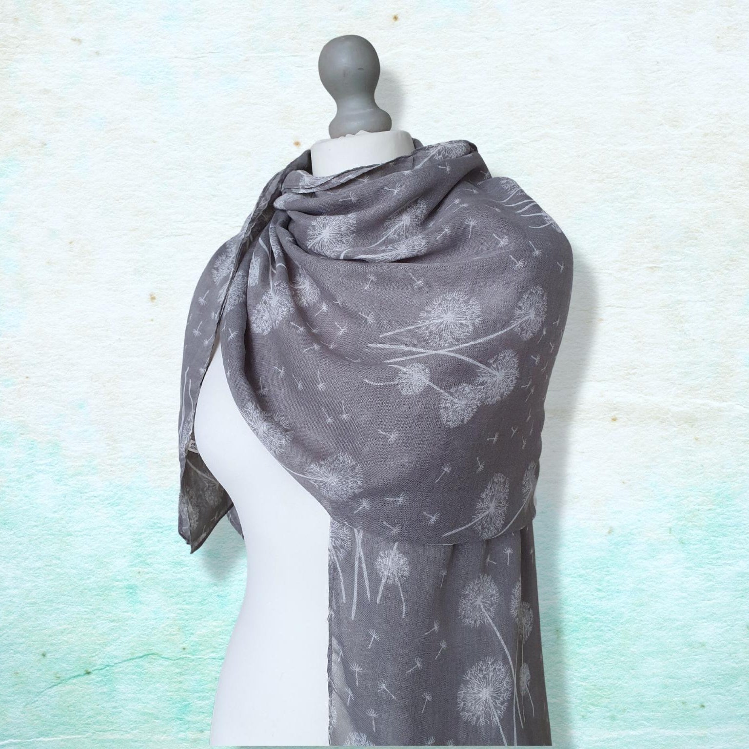 Gray scarf with white dandelion patterns on a mannequin against a light blue textured background