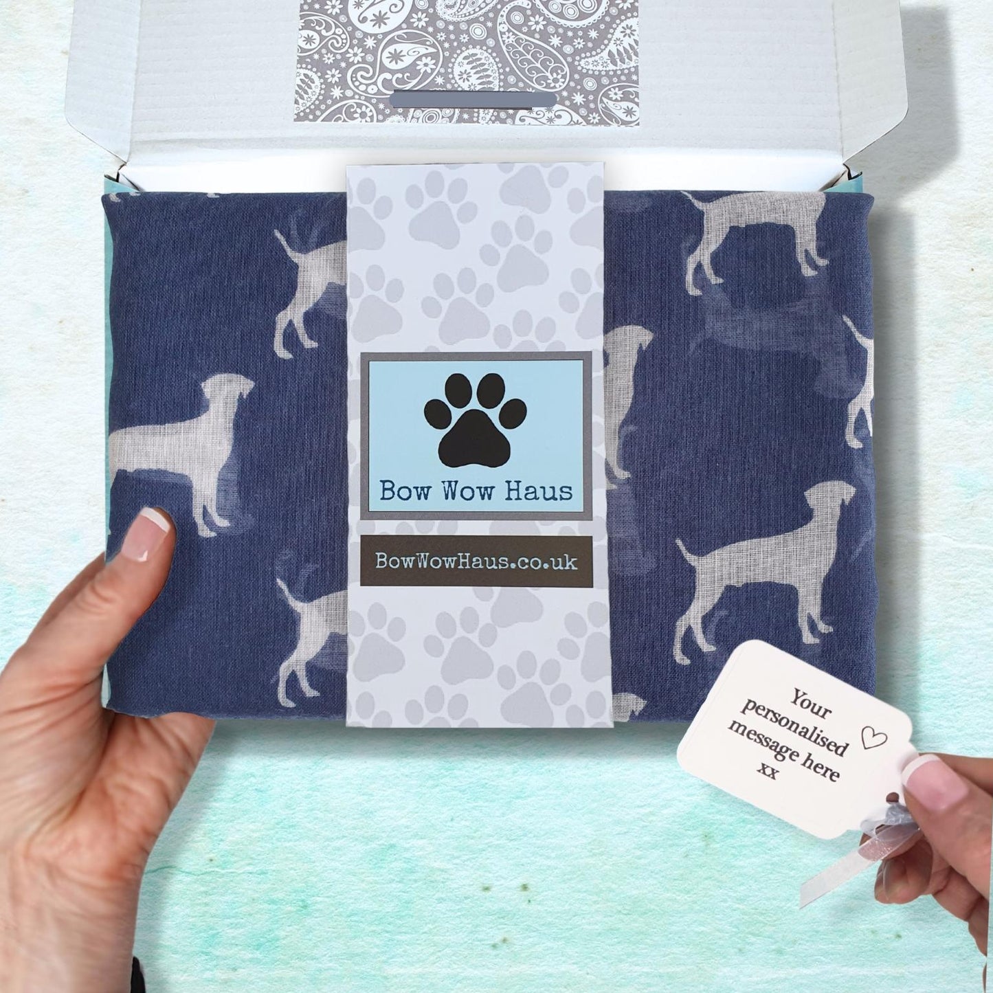 Dog print scarf in a box with a personalised message tag, held by a hand against a light blue background.