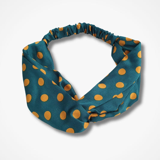 A fabric headband with a twisted knot design, featuring a green background with mustard yellow polka dots, shown on a light grey background.