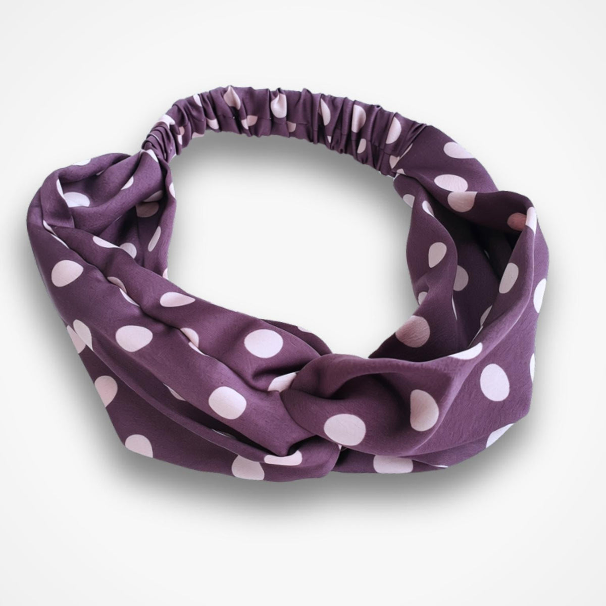 A fabric headband with a knotted twist design, featuring a mauve base with light pink polka dots, shown on a clean white background.