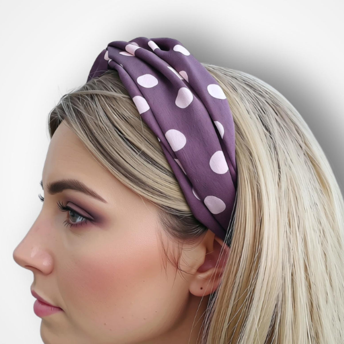 A woman in profile wearing a gathered purple fabric headband with white polka dots, shown against a plain light gray background.
