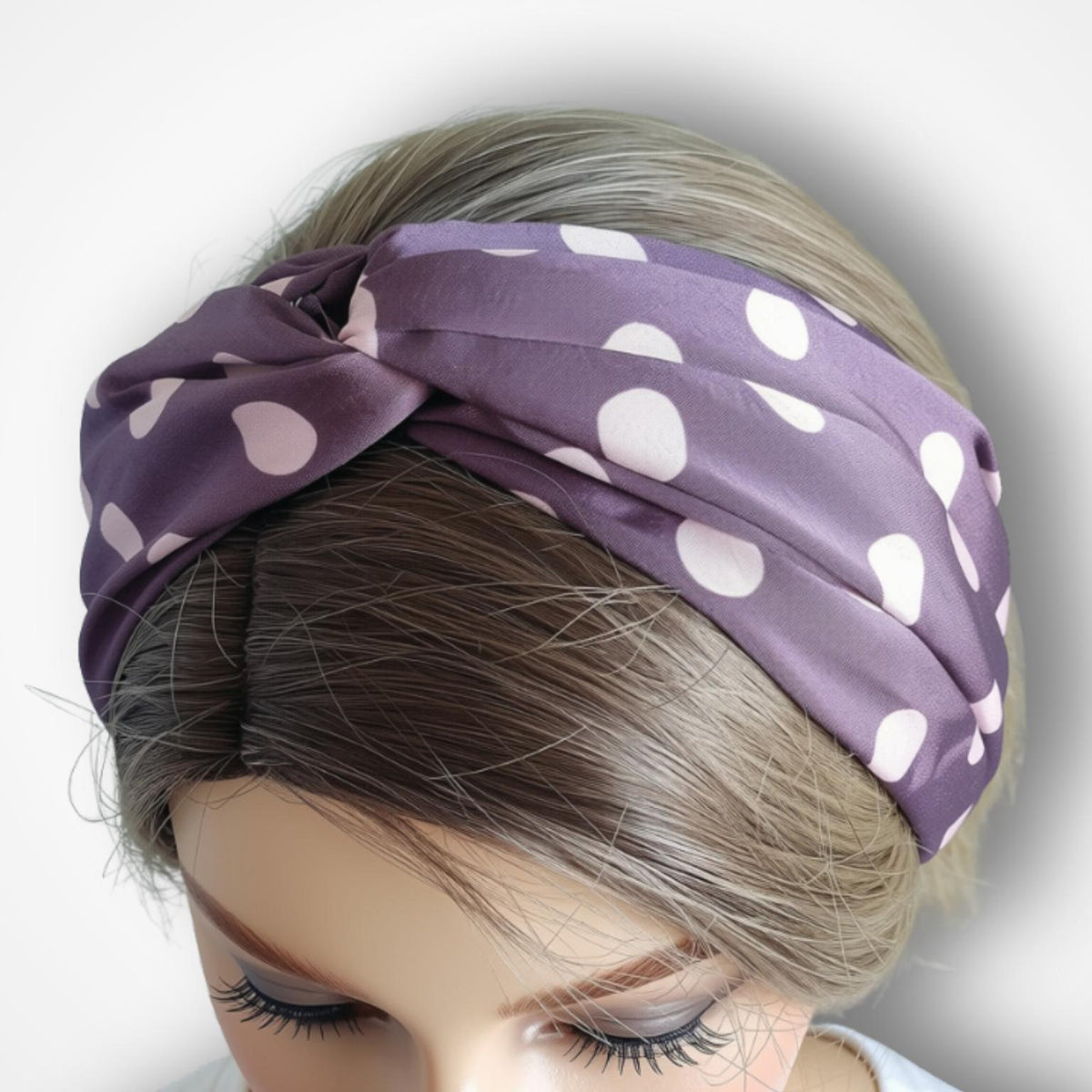 A purple silk-like headband with pink polka dots, styled on a mannequin head with brown hair against a light gray background.
