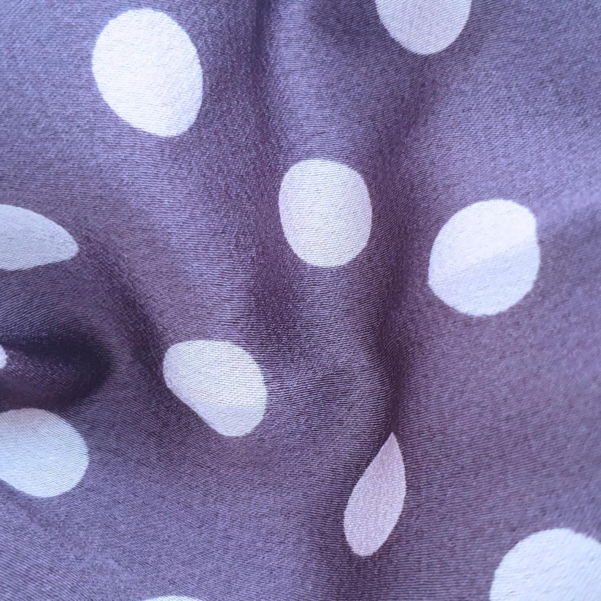A close-up of fabric with a dark purple base and large pink polka dots, showing the material's texture and drape.