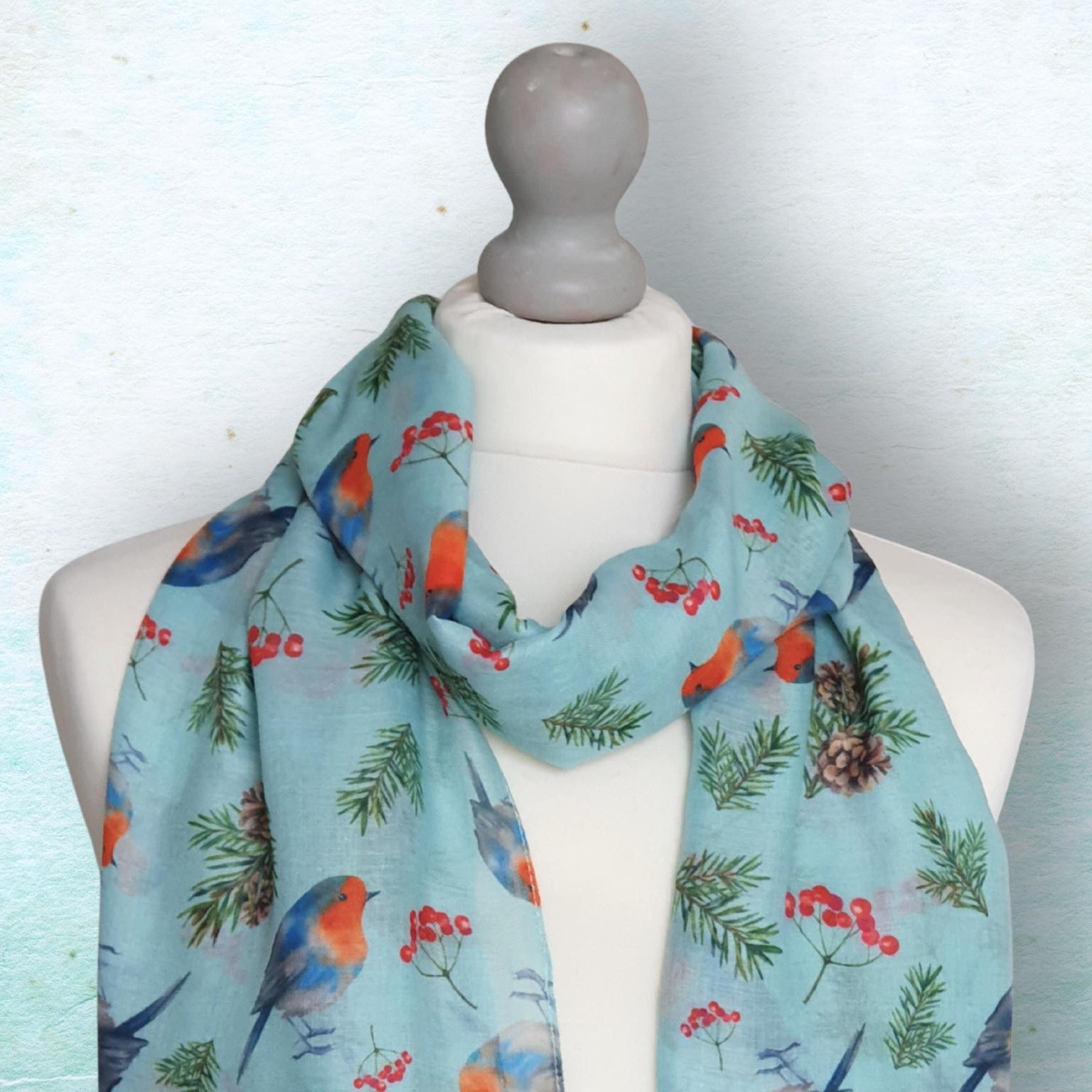 Scarf with robin bird and berry pattern on a mannequin against a light blue background
