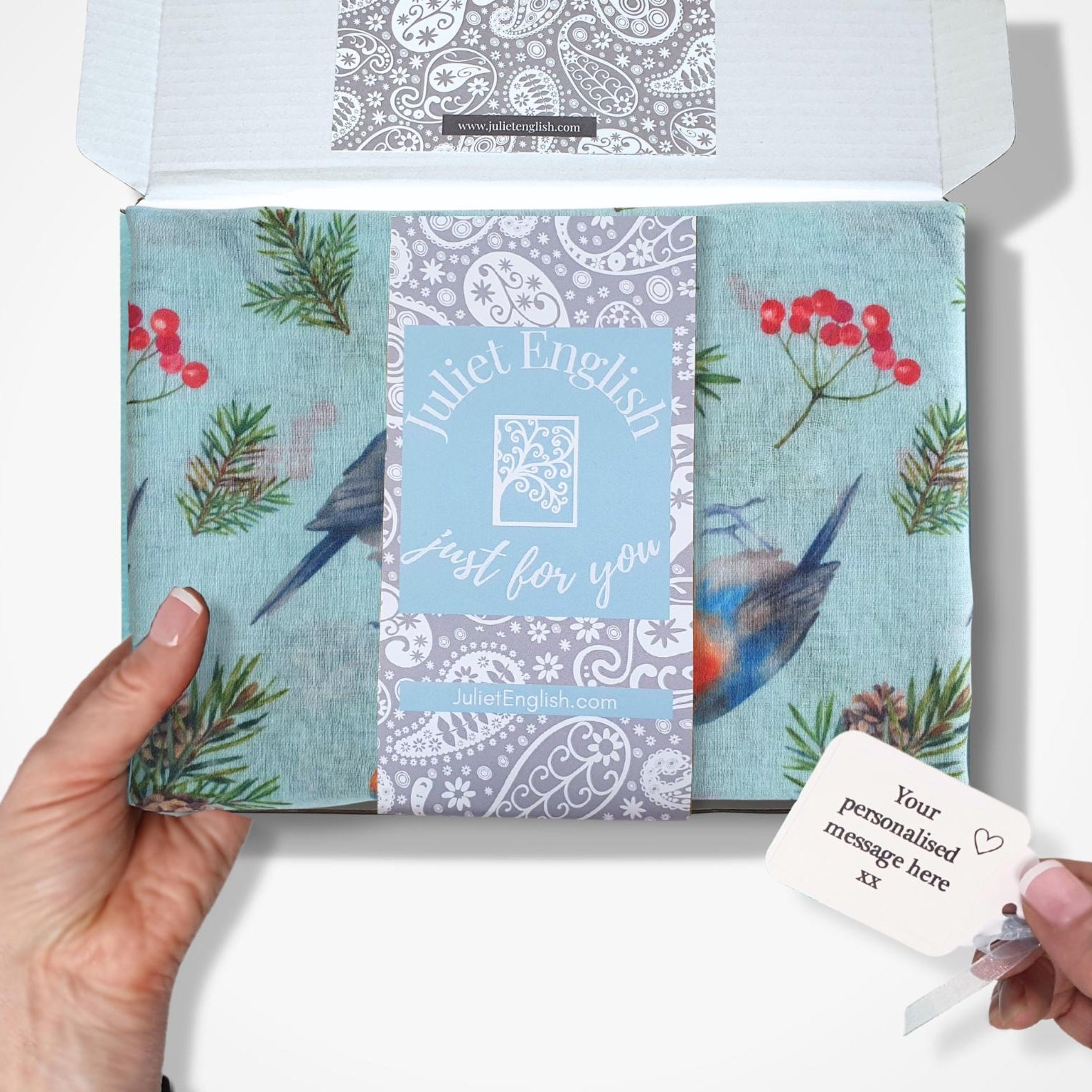 Gift boxed scarf with bird and floral designs, held by a hand.