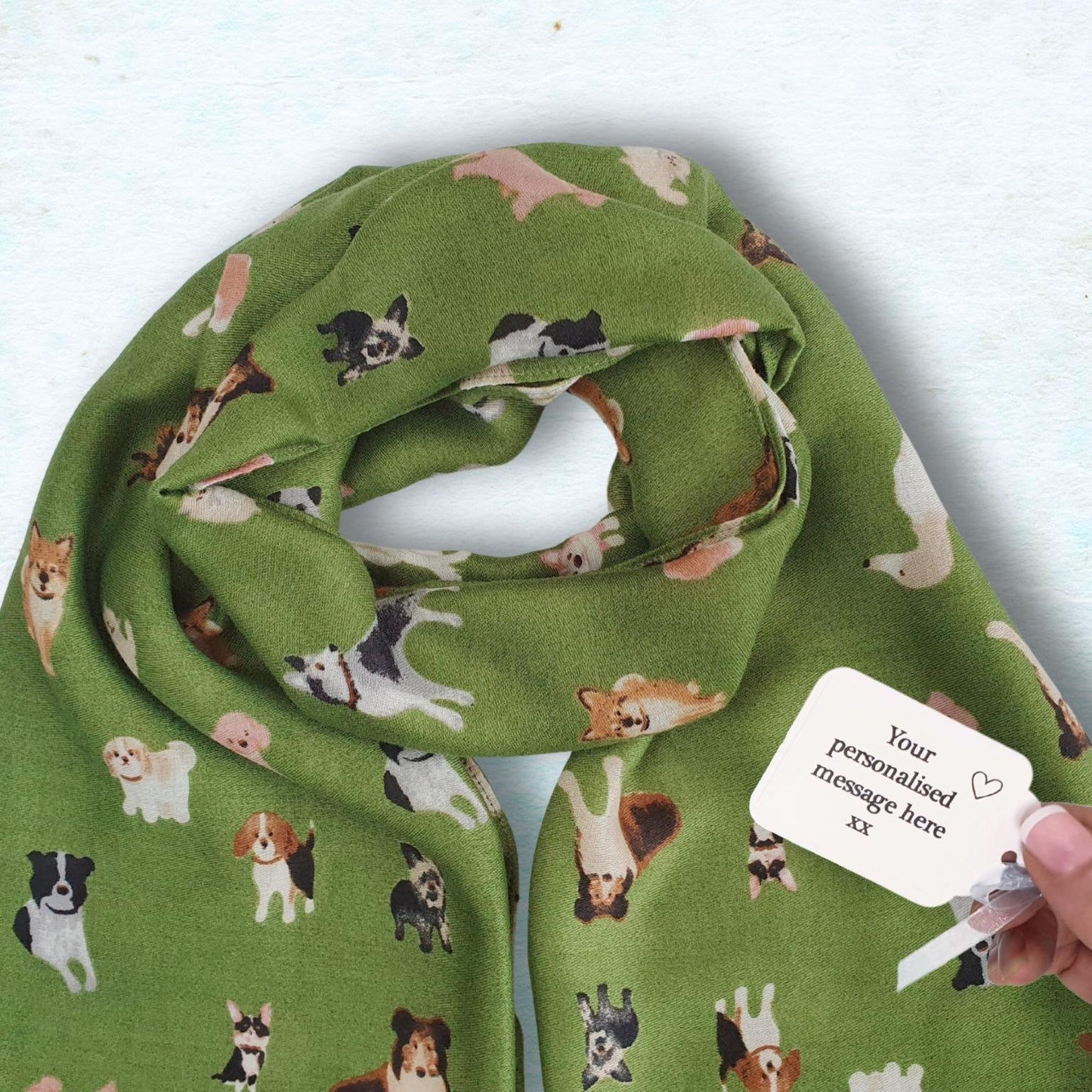 Green scarf with dog pattern held by a hand against a light blue background